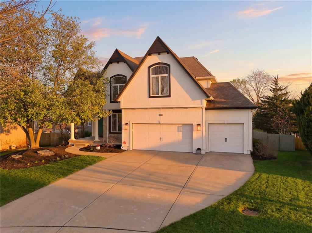 Two-story white house with steep gables, double garage, and broad driveway in warm evening light.