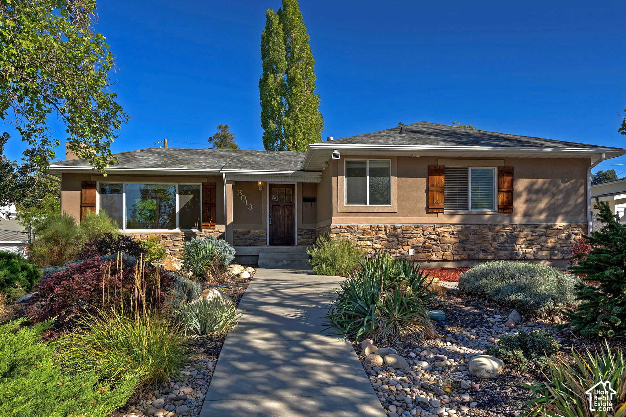Single-story brown home with stone veneer, wood shutters, and a landscaped rock garden.