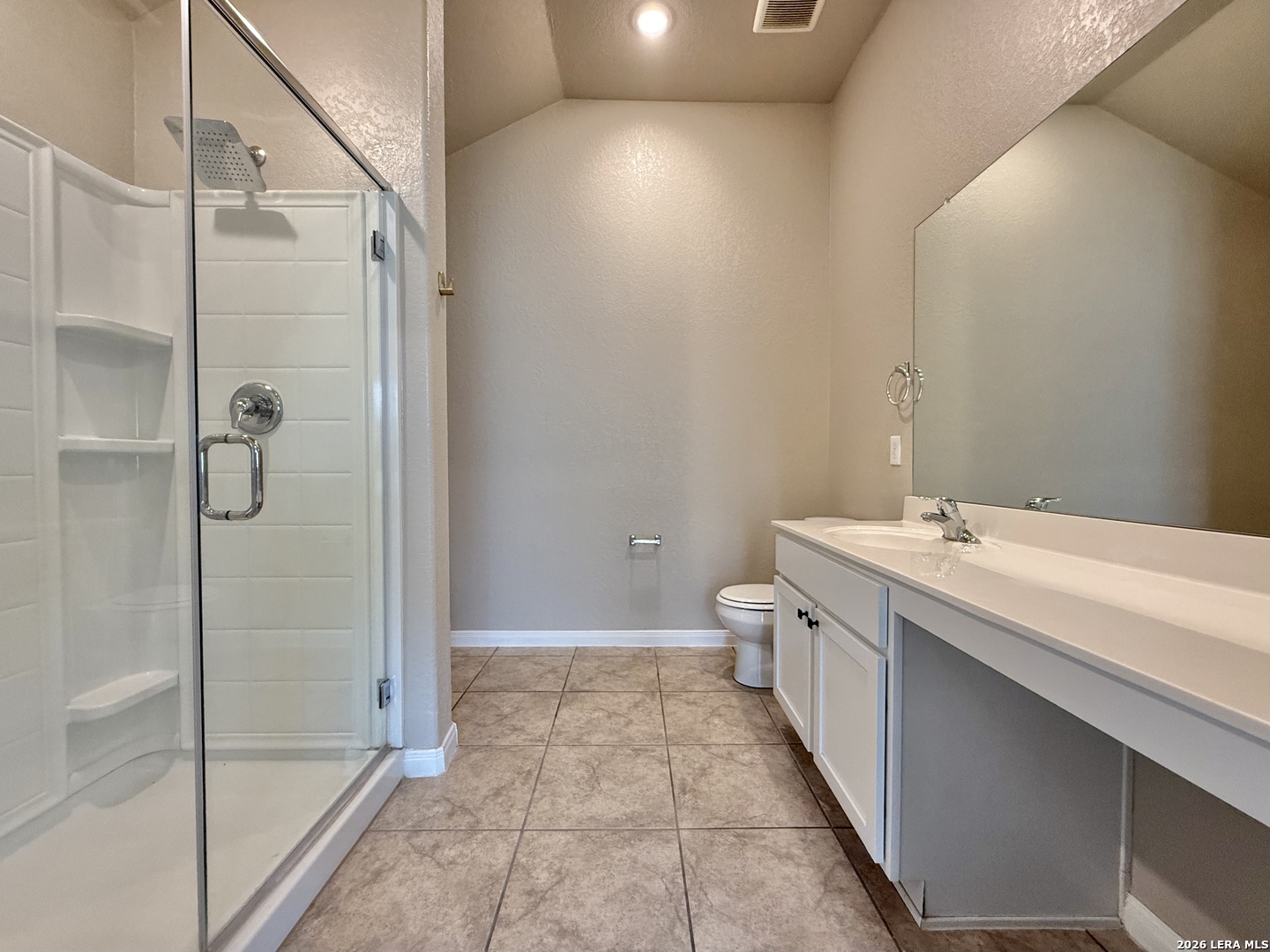 Bathroom with a glass shower, long white vanity, large mirror, and brown tile floor.