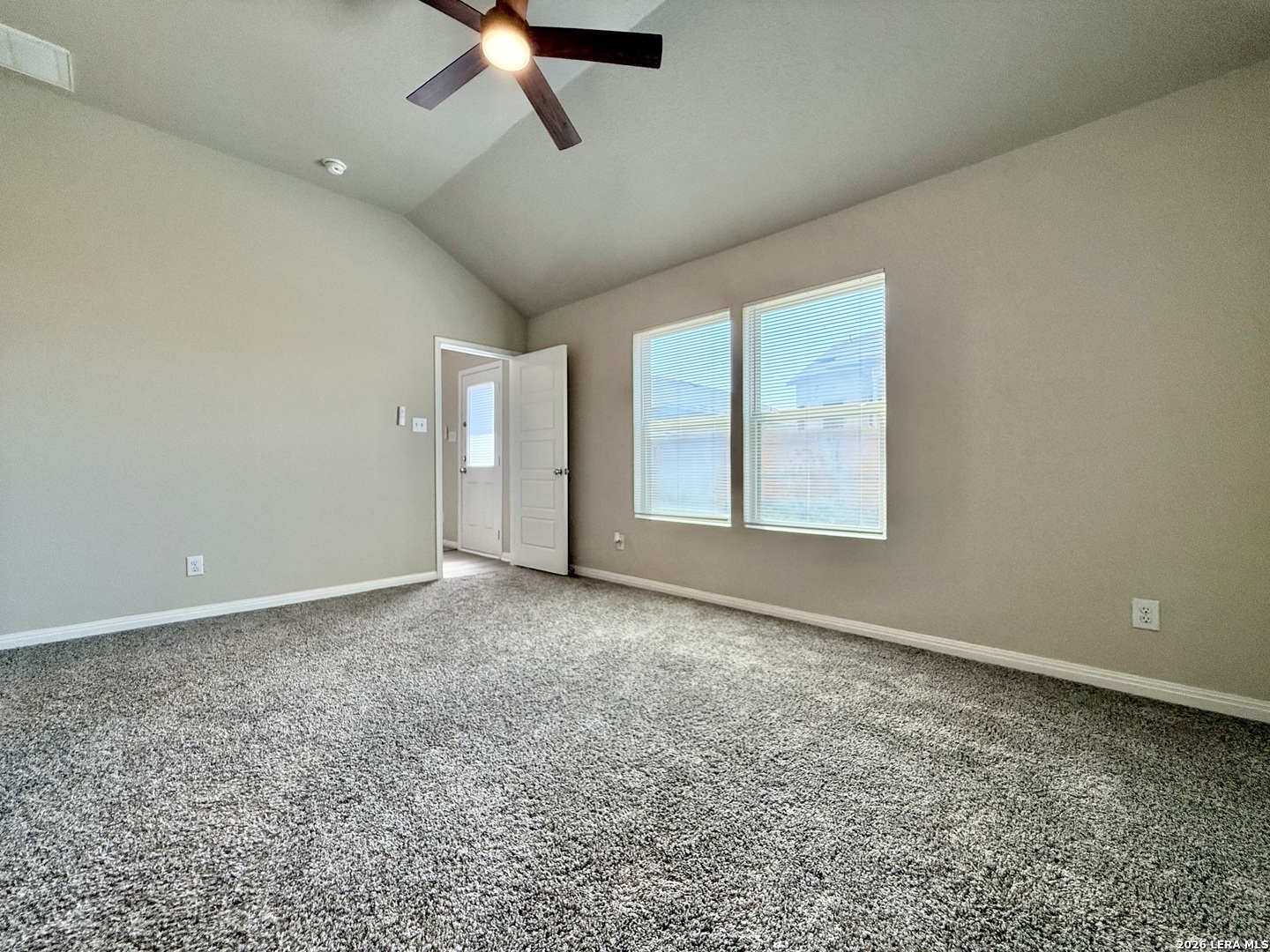 Vacant bedroom with gray carpeting, two windows, and a ceiling fan with light.