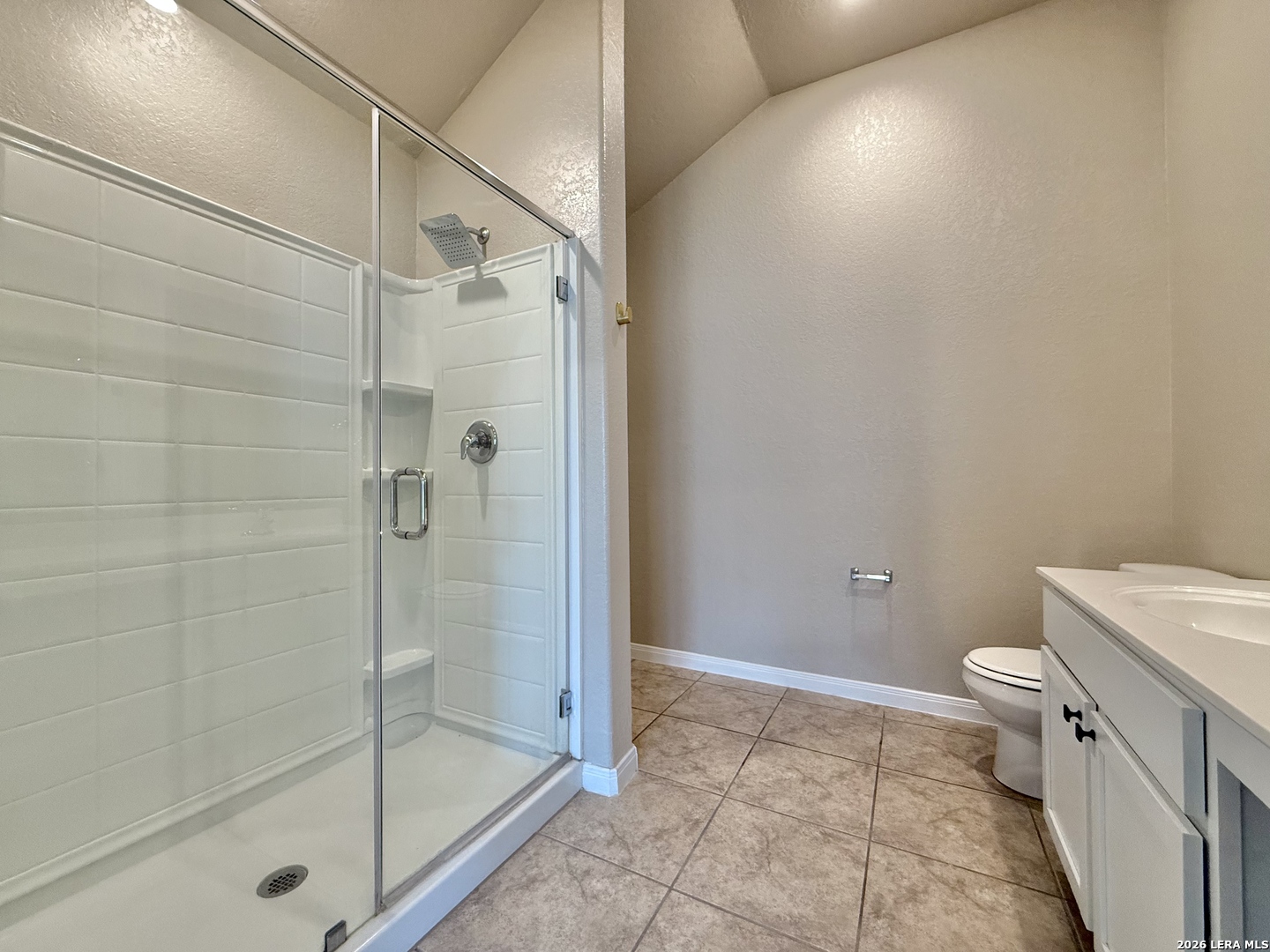 Bathroom with a glass-enclosed tiled shower, white vanity, and brown tile floor.