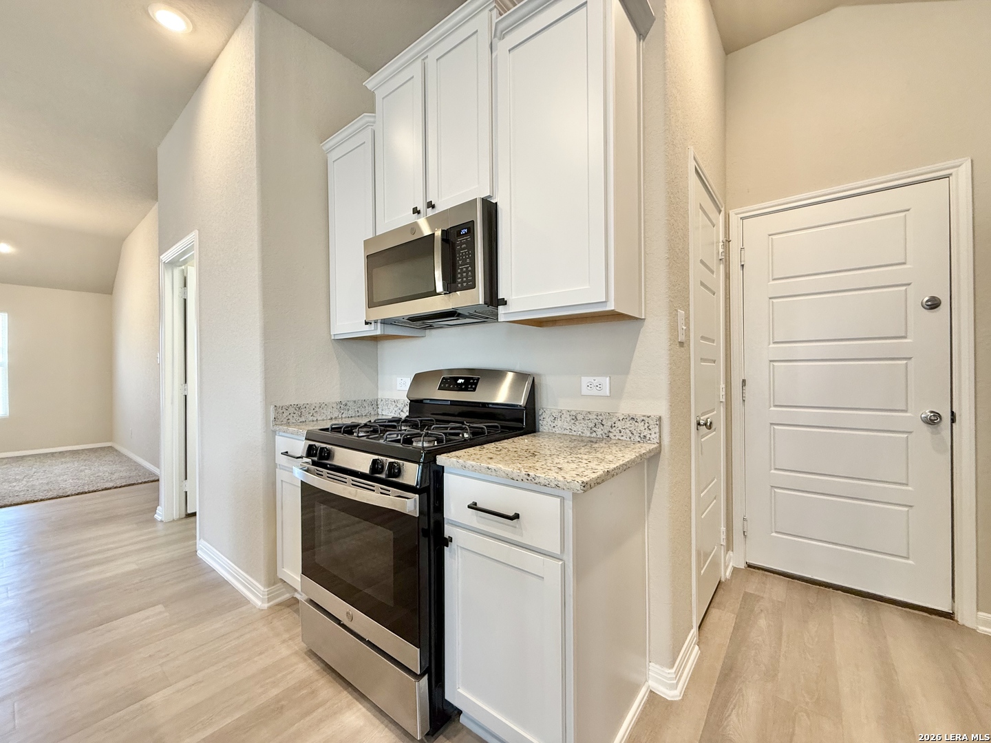 Kitchen with white cabinets, granite counters, and stainless steel gas range and microwave.