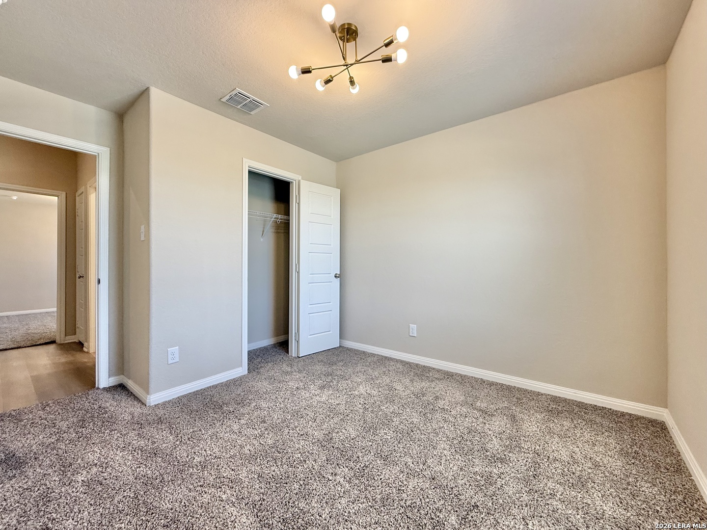 Empty carpeted bedroom with an open closet and brass ceiling light.