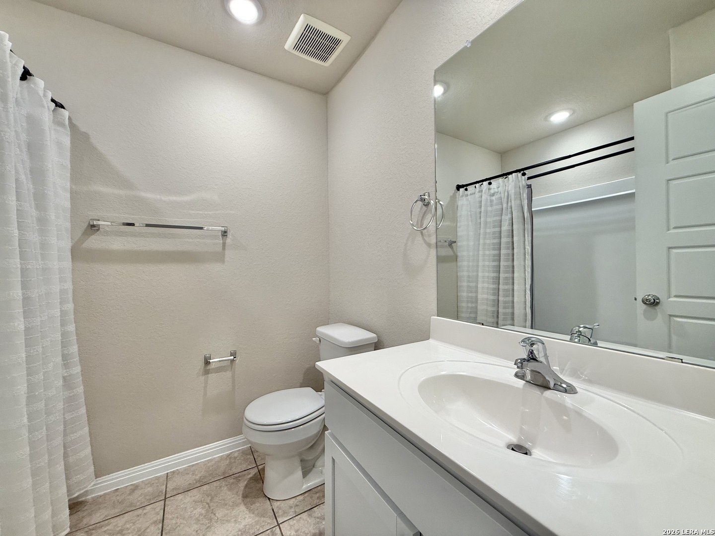 Bathroom with a white vanity, toilet, and curtained tub or shower reflected in a large mirror.