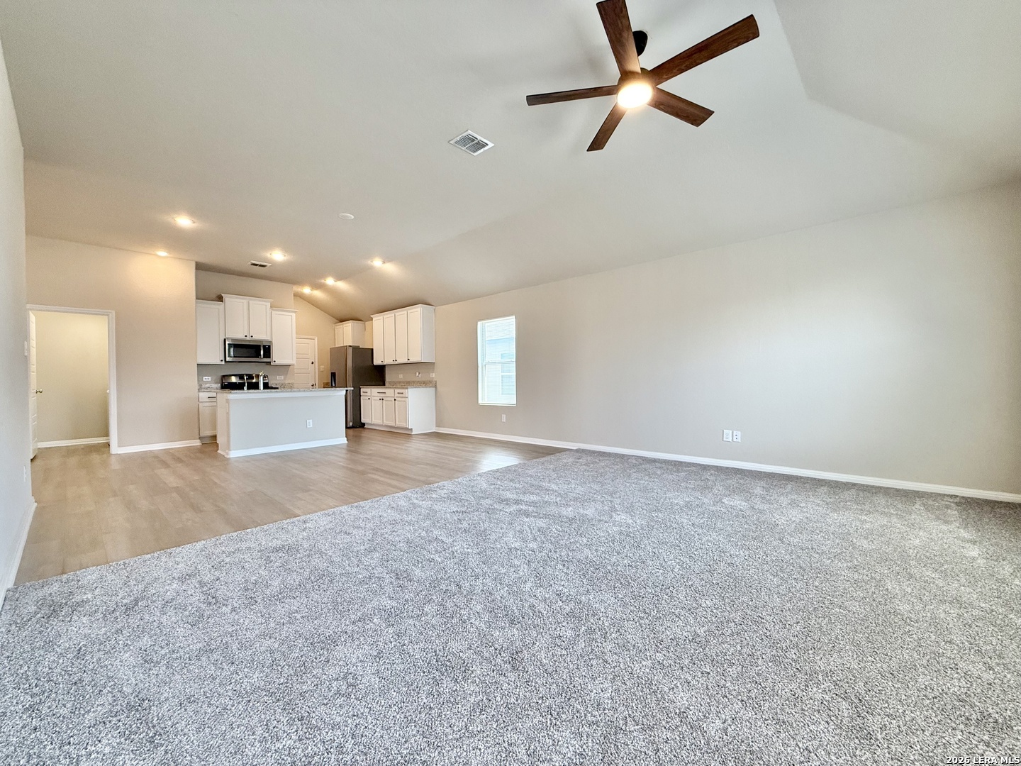 Open-plan living room and kitchen with gray carpet, white cabinets, and a wood ceiling fan.