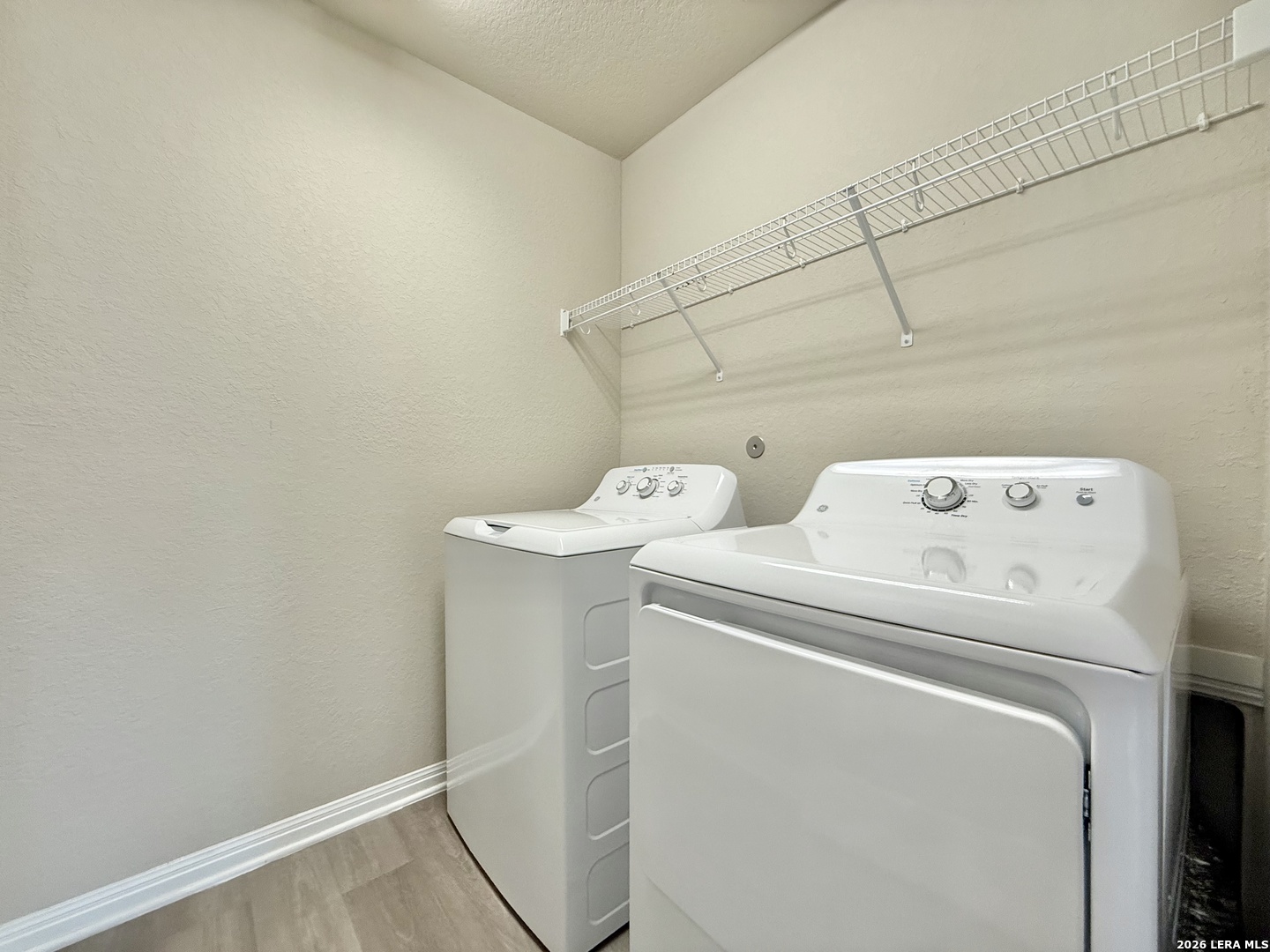 Laundry room with a white washer and dryer beneath a long wire shelf.
