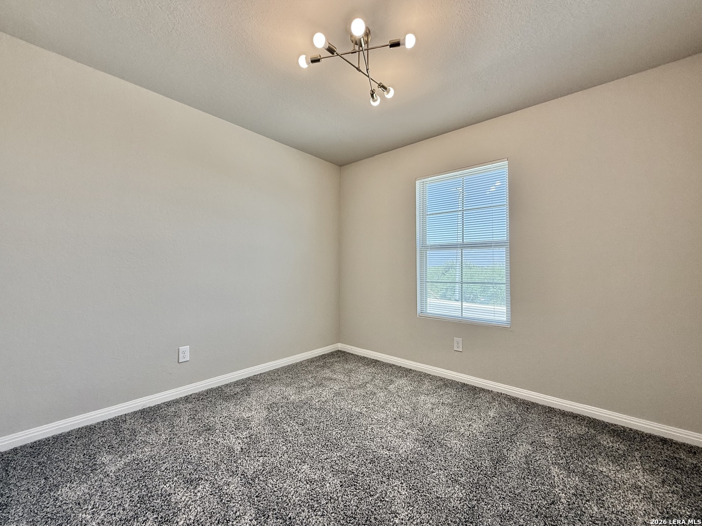 Empty bedroom with gray patterned carpet, window blinds, and a modern ceiling light.