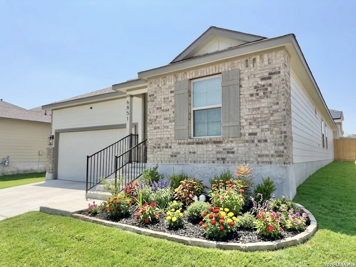 Single-story brick-front home with an attached garage and colorful flower garden.