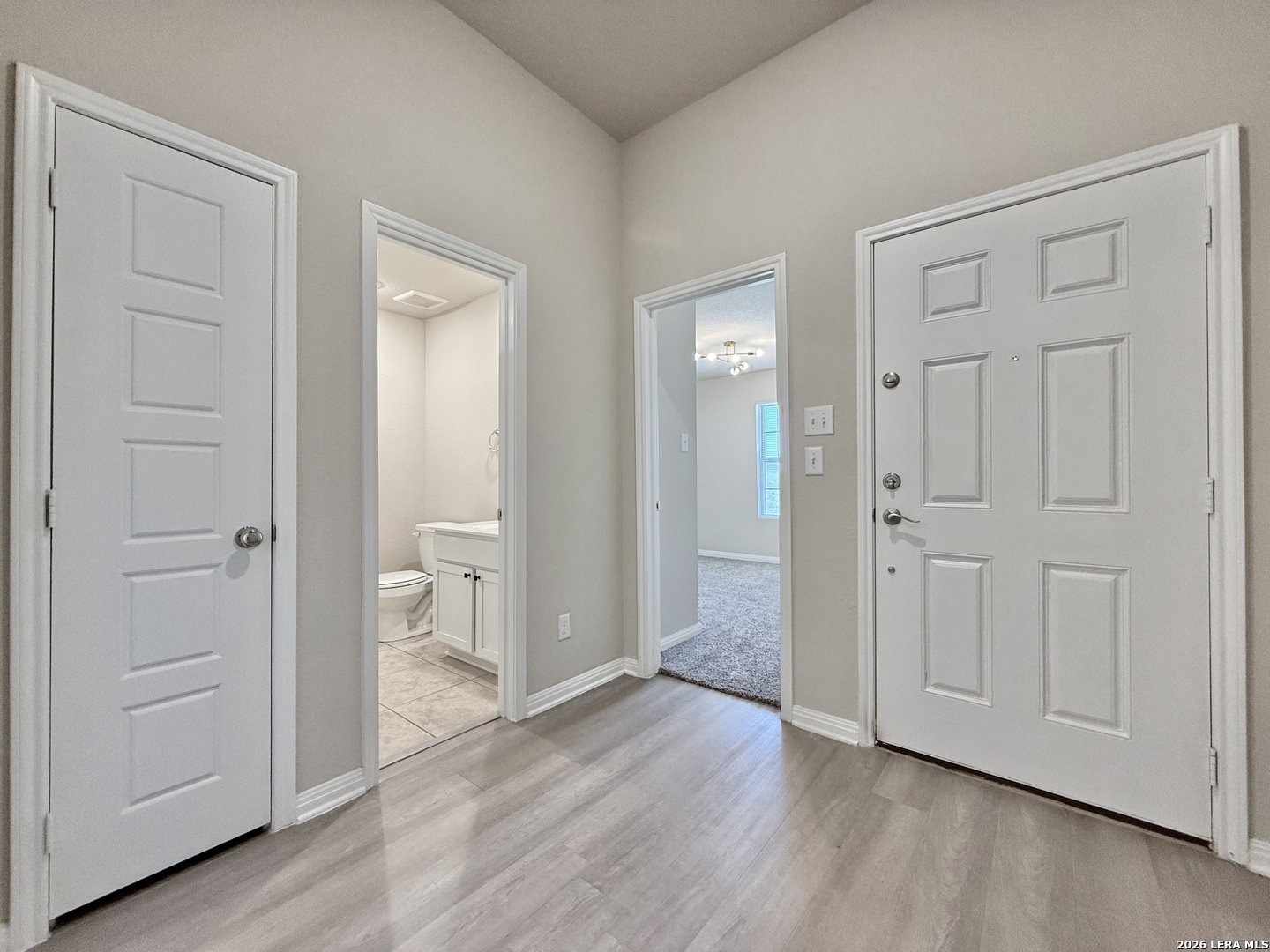 Unfurnished entry foyer with gray flooring, a white front door, and open views into a bathroom and carpeted room.