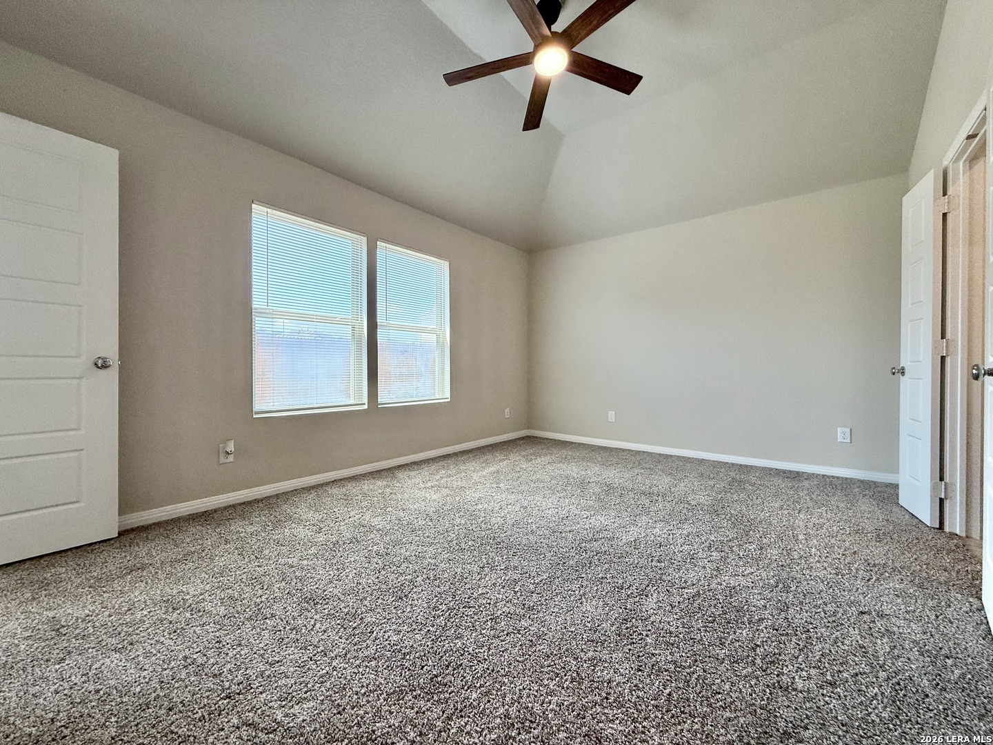 Vacant bedroom with gray carpet, two windows with blinds, and a ceiling fan.