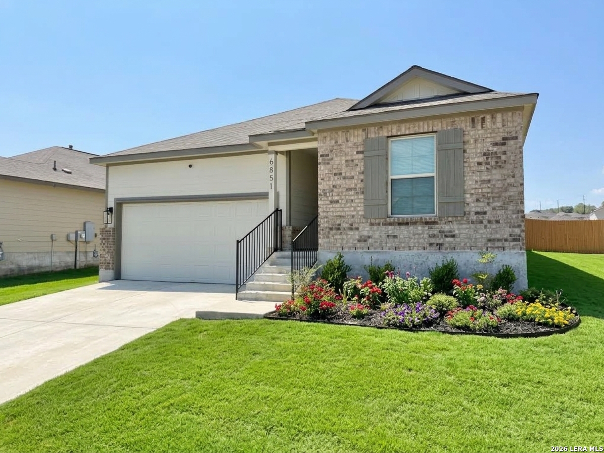 Single-story brick home with a two-car garage, broad lawn, and colorful front flower bed.