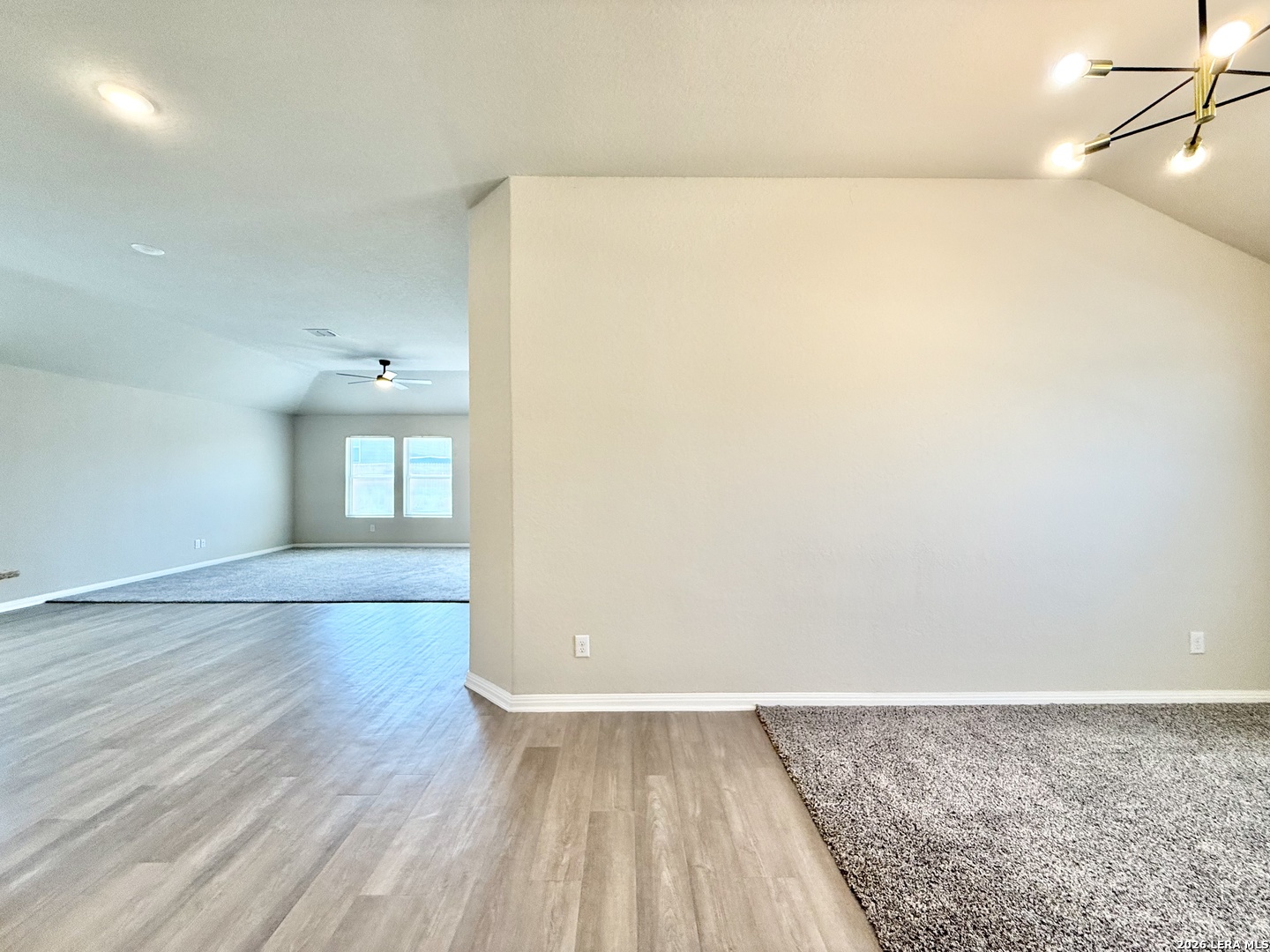 Empty open-plan living area with wood-look flooring, carpeted section, and two windows.