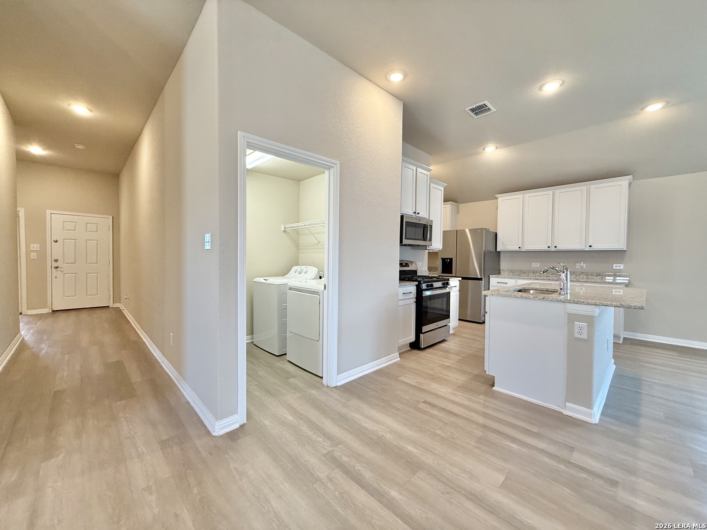 Vacant kitchen and entry with white cabinets, a granite island, and an open laundry closet.