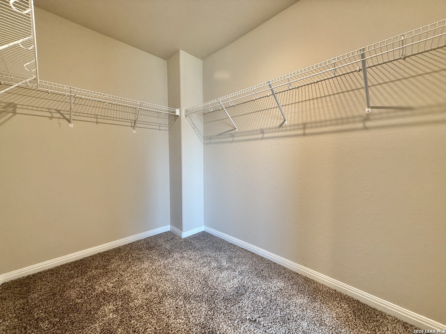Empty walk-in closet with white wire shelving and brown carpet.