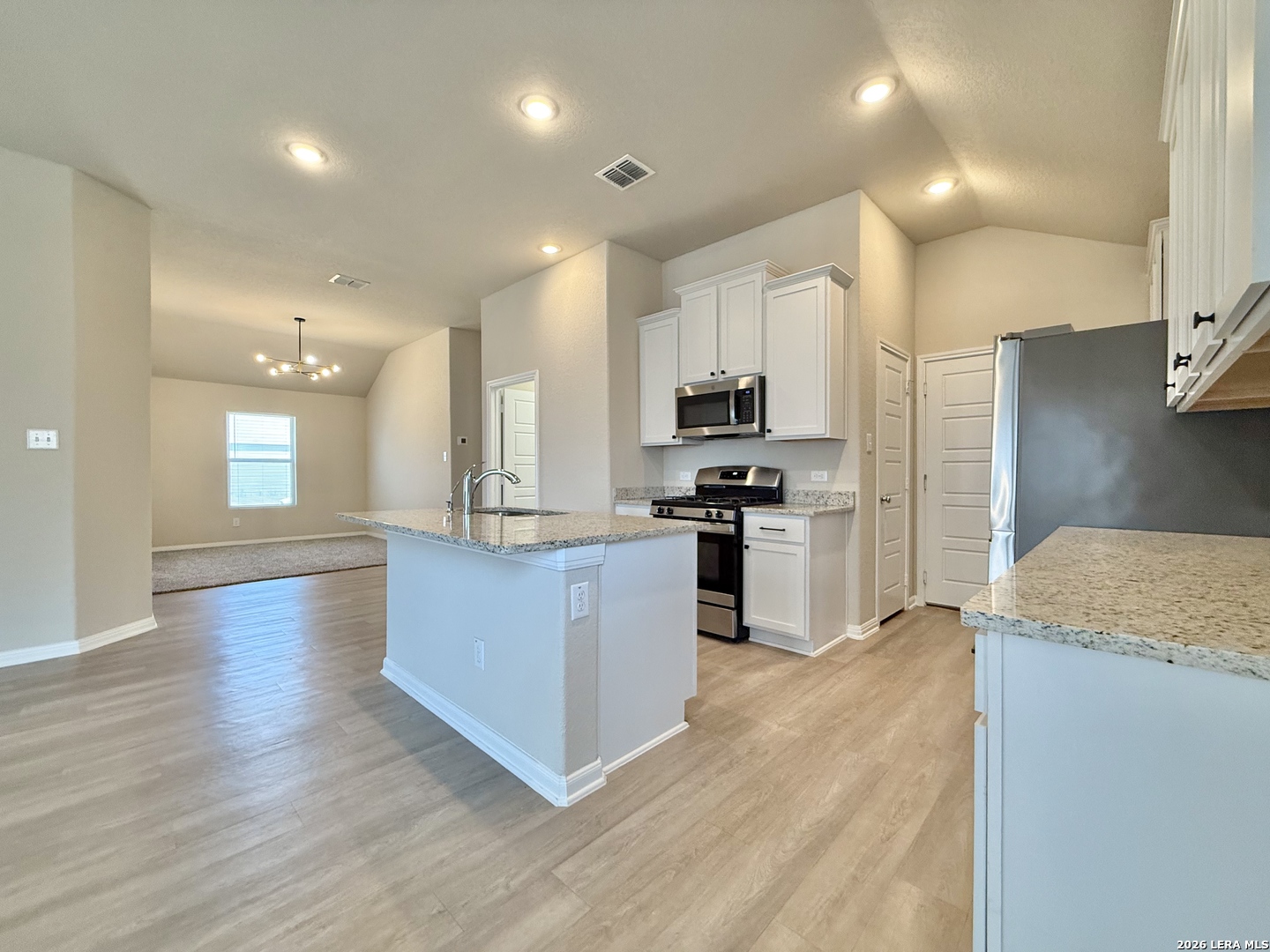 Open kitchen with white cabinets, stainless appliances, granite counters, and a central island.