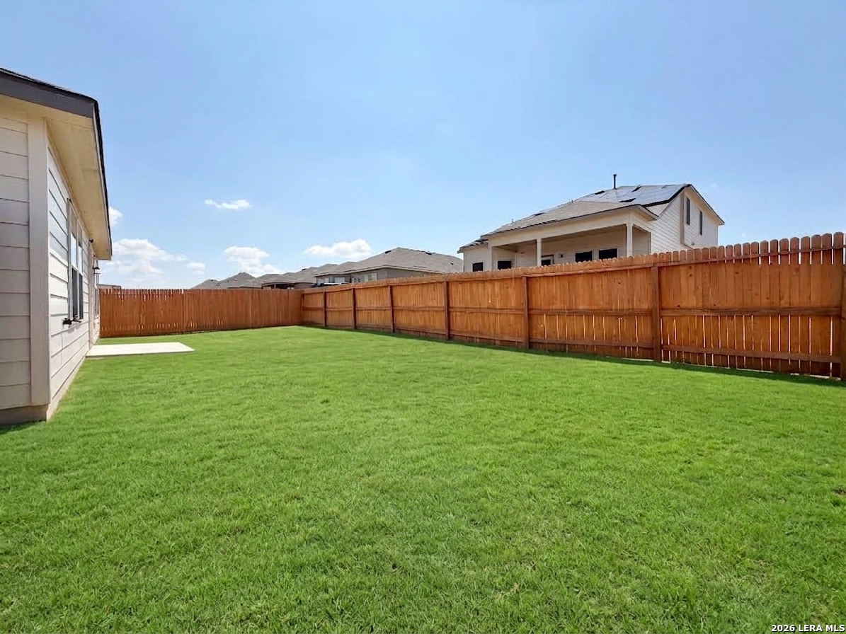 Grassy backyard with a tall wooden privacy fence and a small concrete patio beside the house.