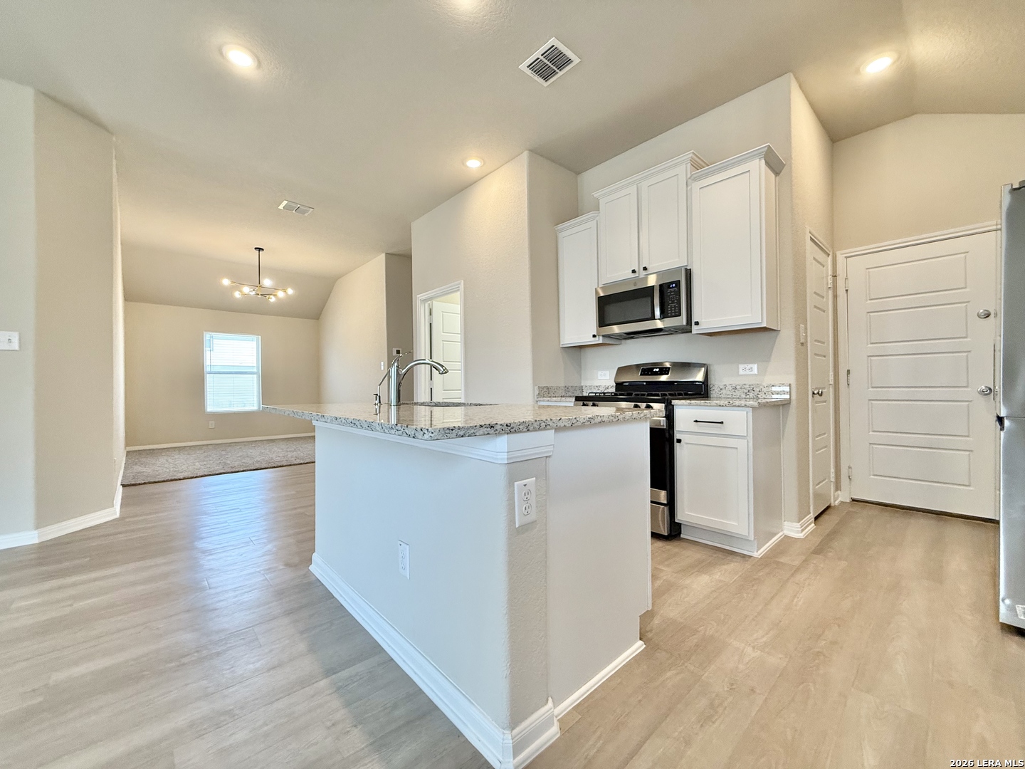 Vacant kitchen with white cabinets, stainless steel appliances, granite counters, and a large peninsula.