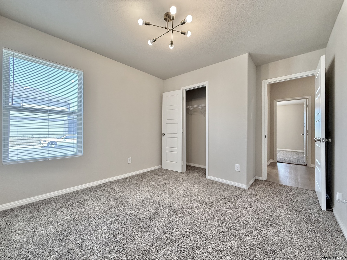 Empty bedroom with gray carpet, a window with blinds, an open closet, and a modern ceiling light.