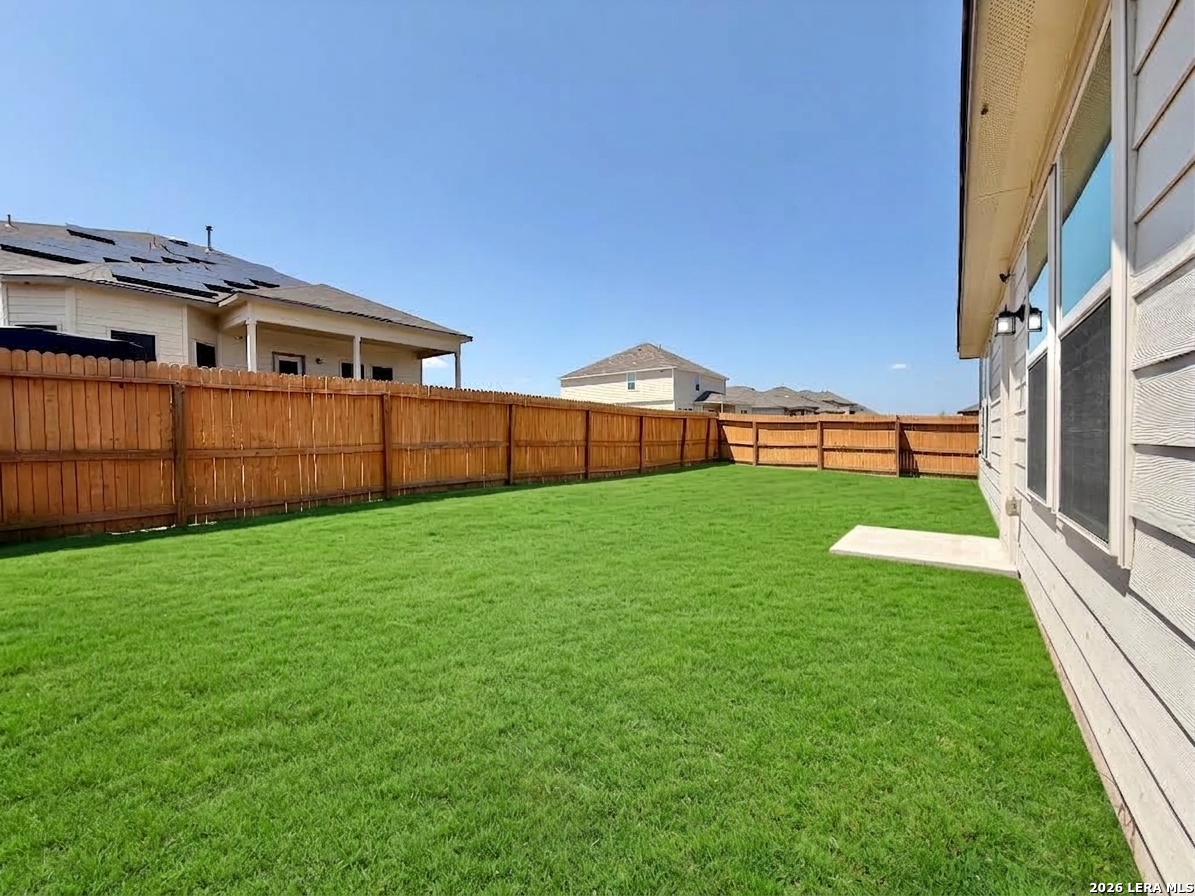 Fenced backyard with a broad green lawn and wooden privacy fence beside the house.