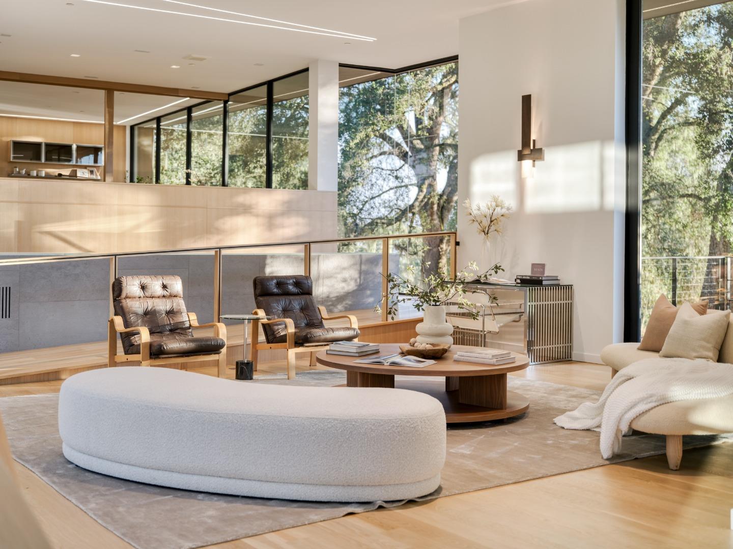 Contemporary living room with leather lounge chairs, an oval ottoman, and tall windows overlooking trees