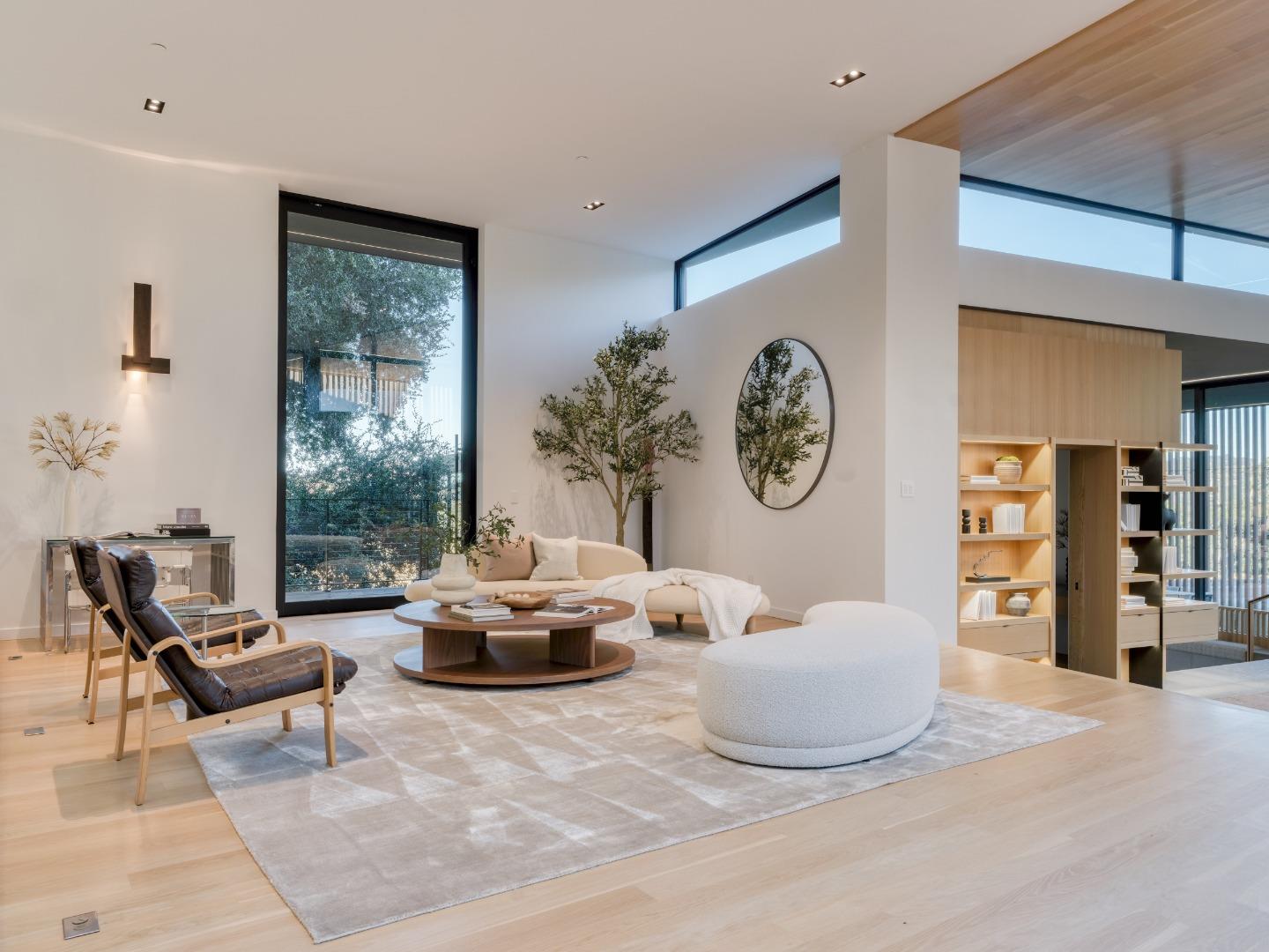 Living room with white sofas, a leather lounge chair, and floor-to-ceiling windows.