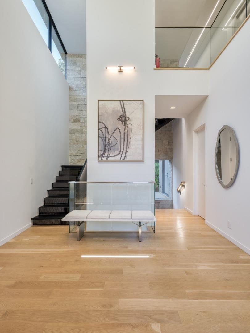 Modern entry hall with a black staircase, glass railing, and bench beneath abstract artwork.