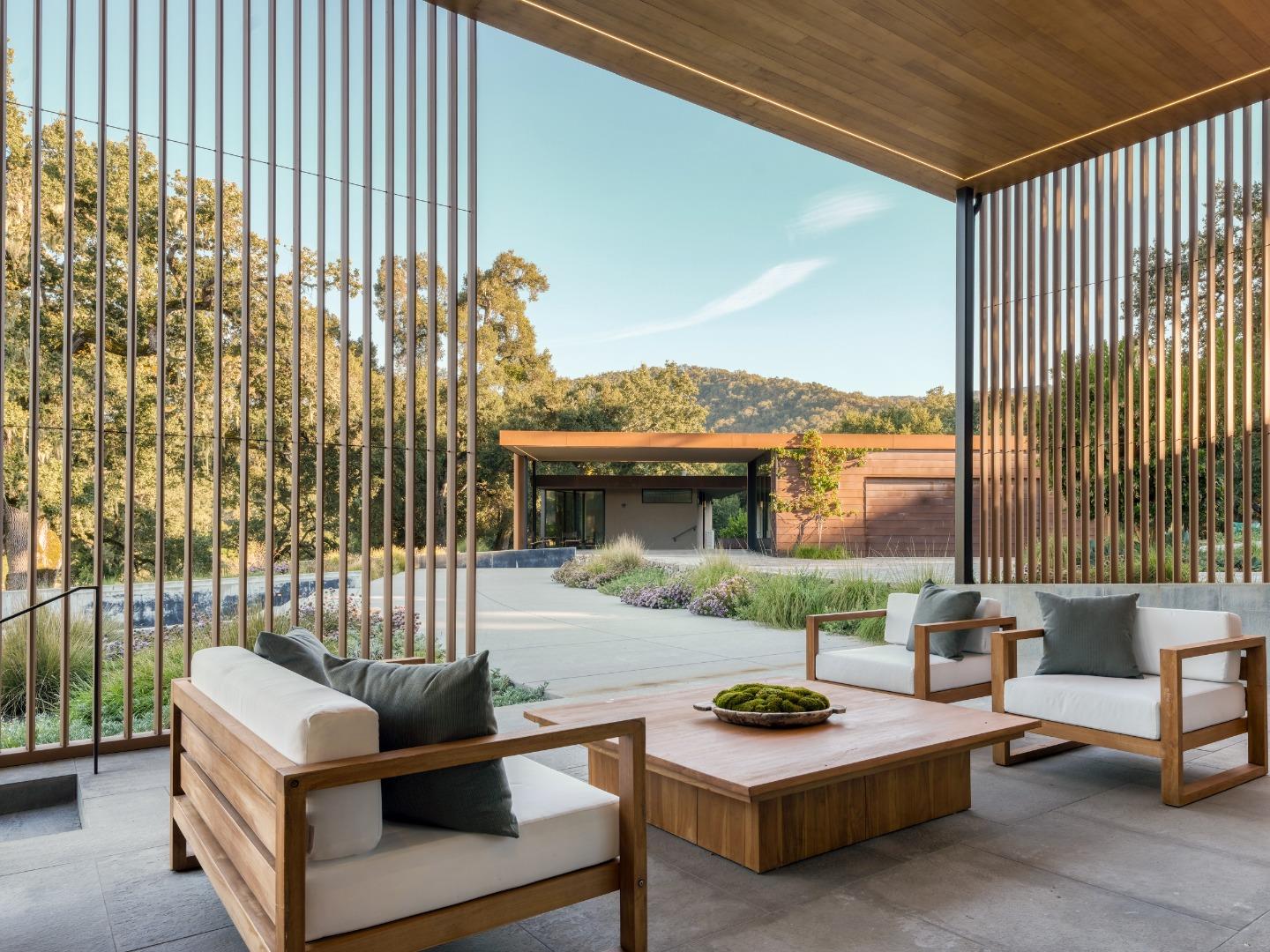 Covered patio with wood-framed lounge seating overlooking landscaped grounds and a modern home.