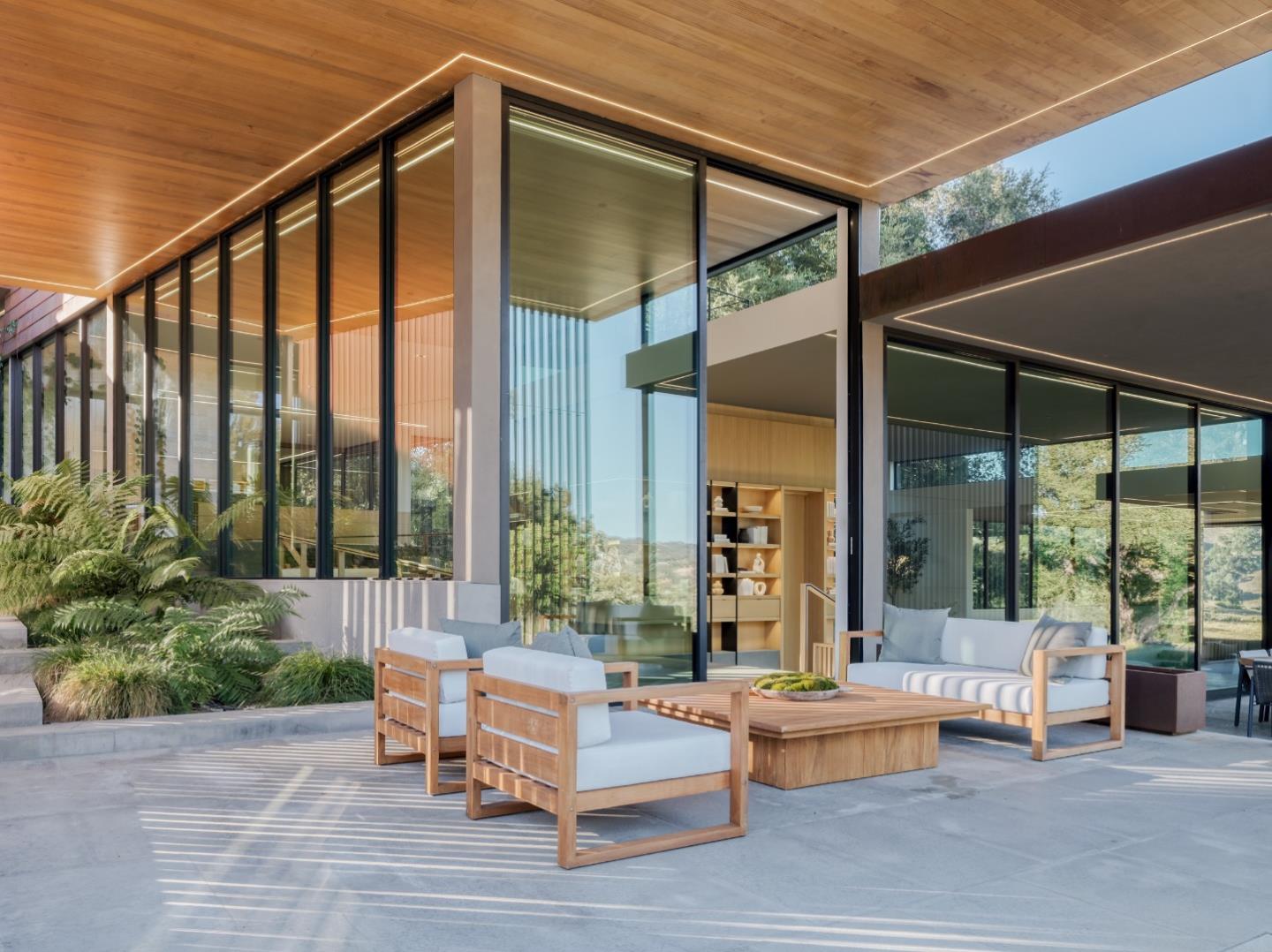Modern home's covered patio with floor-to-ceiling glass walls and wood-framed lounge seating.