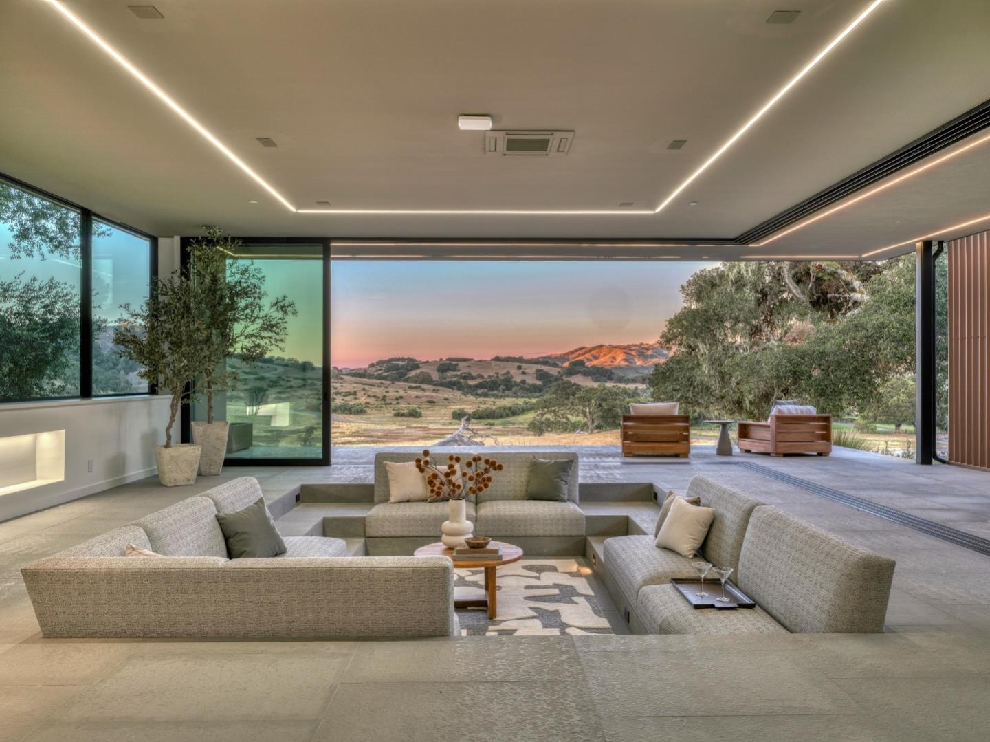Modern sunken living room opening onto a terrace with rolling hills at dusk.