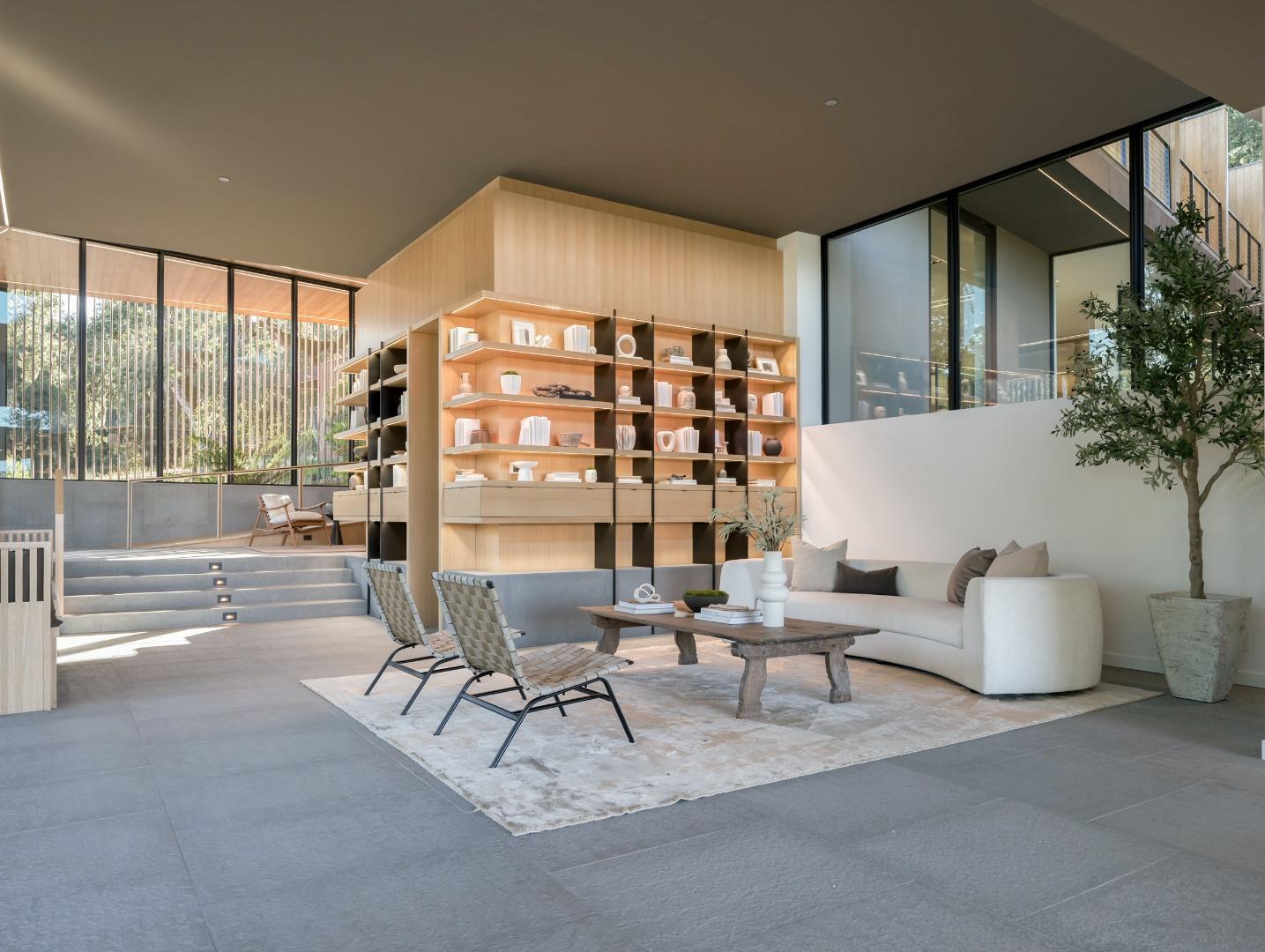 Modern living room with illuminated wood shelving, a curved white sofa, and floor-to-ceiling windows.