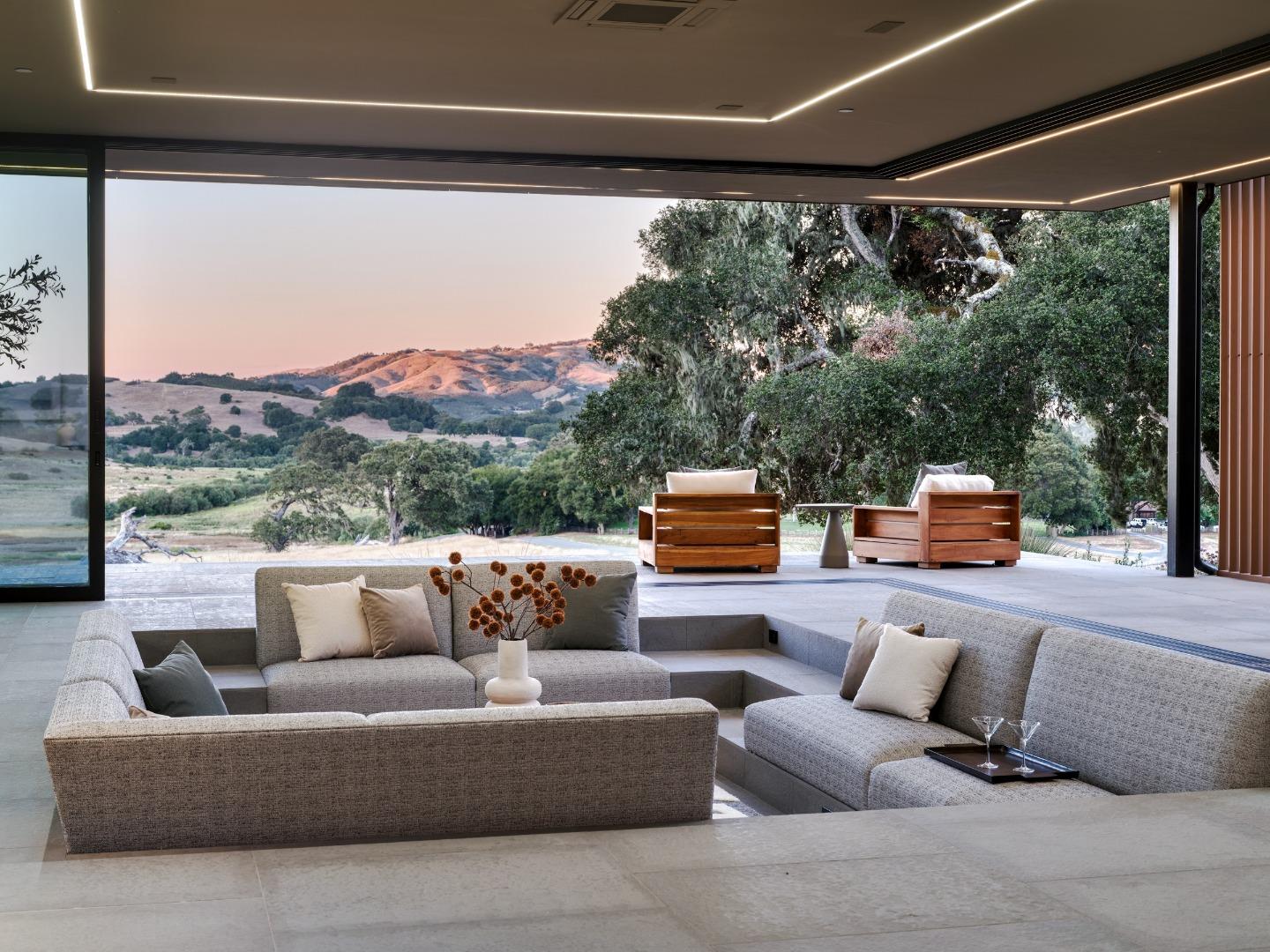 Sunken sectional in an open living area facing a covered terrace, oak trees, and rolling hills.