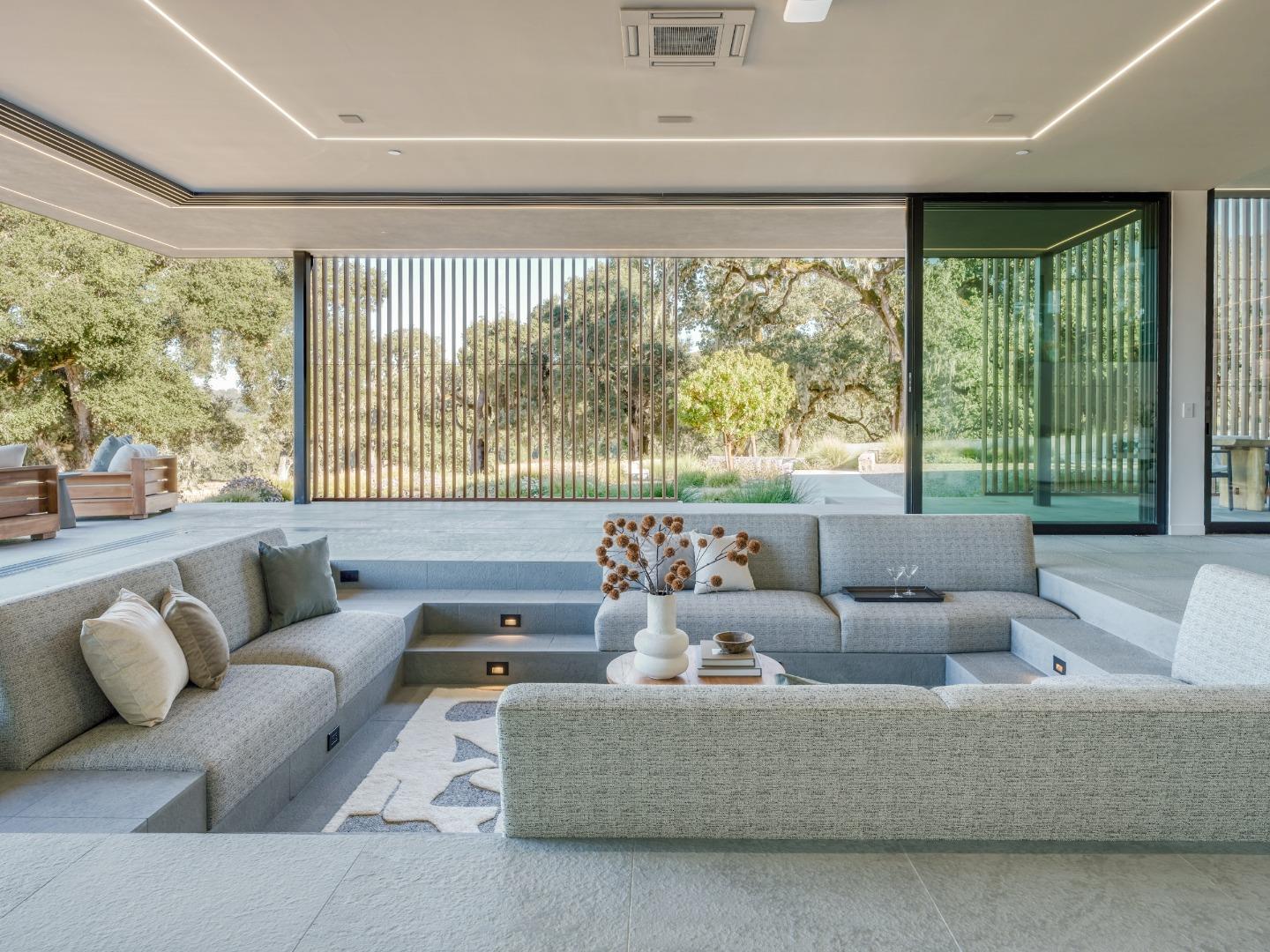 Sunken sectional living room opens through floor-to-ceiling glass doors to landscaped grounds and oak trees.