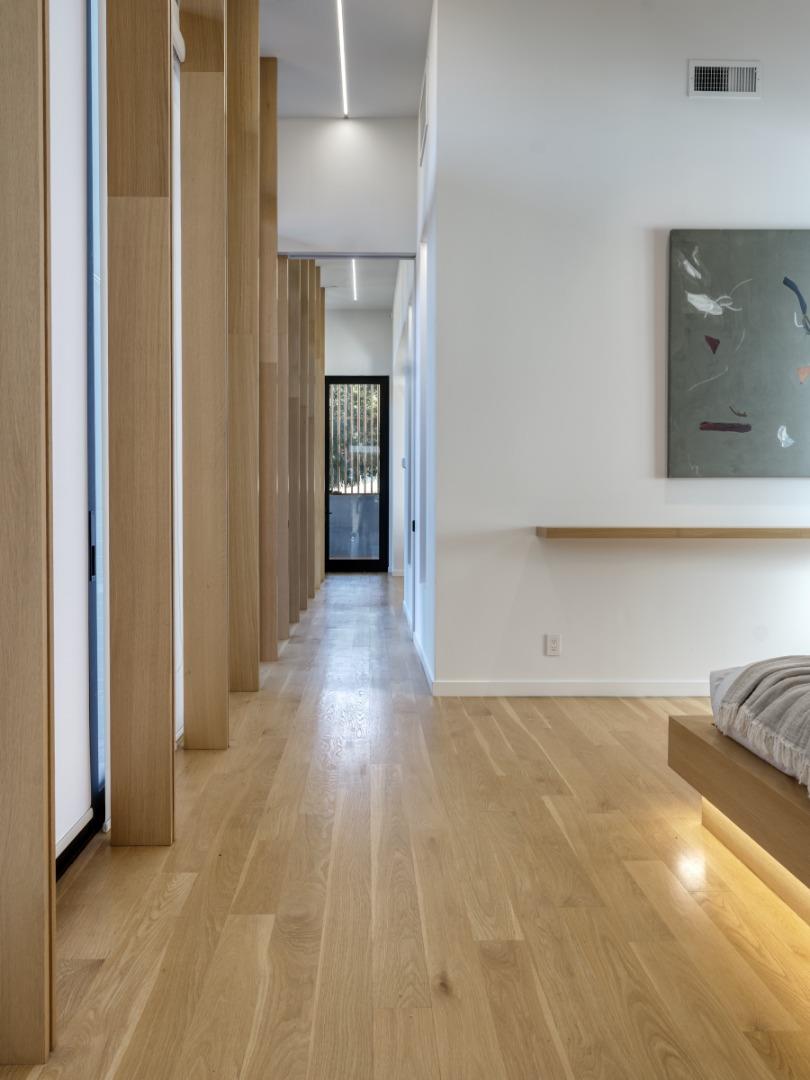 Modern hallway with vertical wood slats and oak floors beside a bedroom with a low bed.
