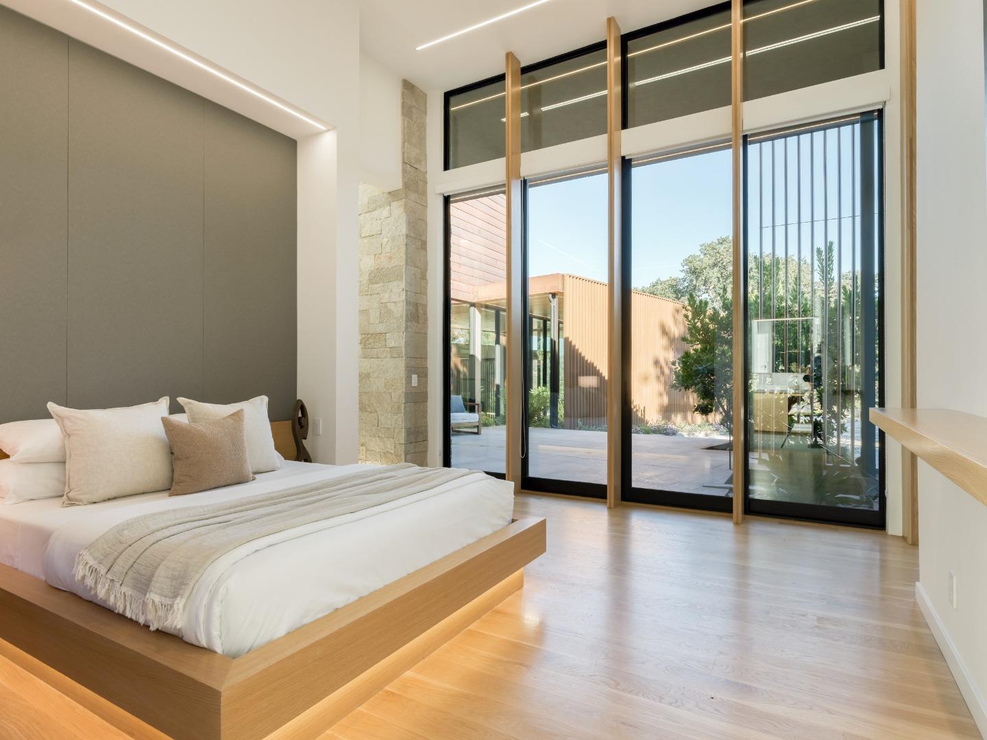 Modern bedroom with a low platform bed and floor-to-ceiling windows overlooking a courtyard.