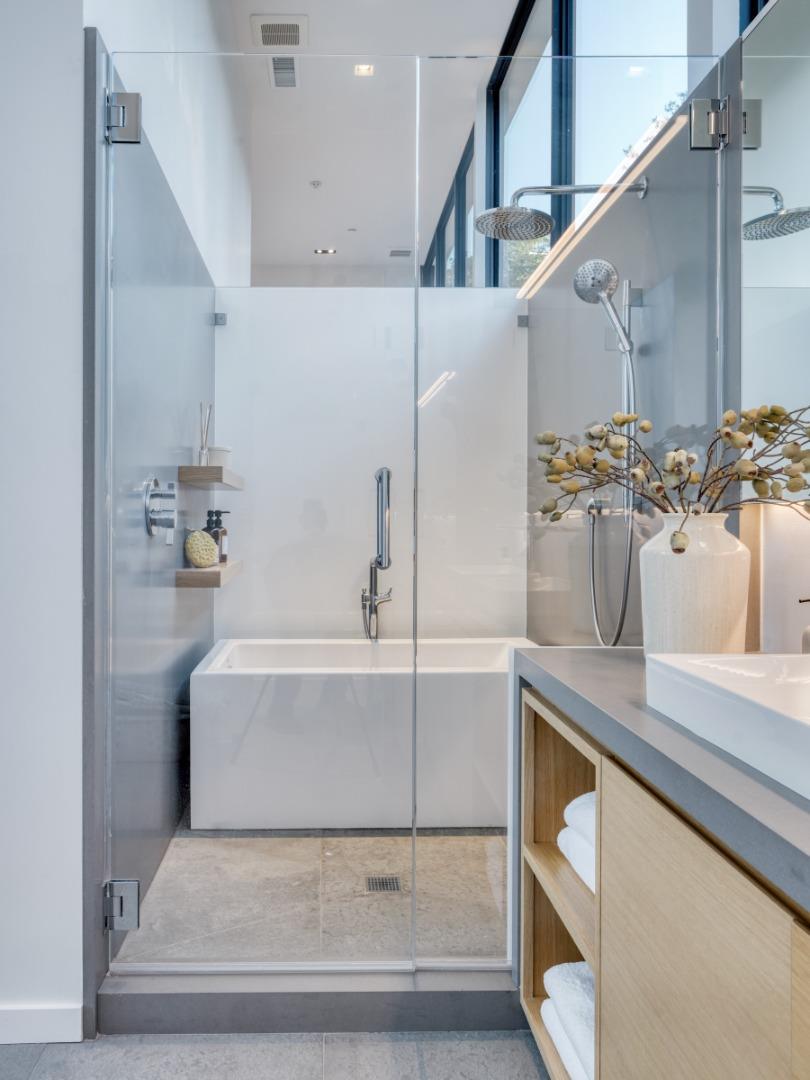 Modern bathroom with a glass-enclosed shower, soaking tub, and pale wood vanity.