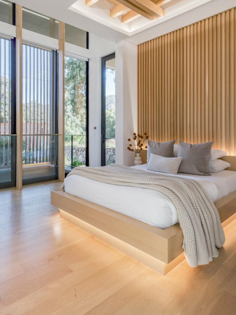Bedroom with a light-wood platform bed, slatted wood accent wall, and tall glass doors.