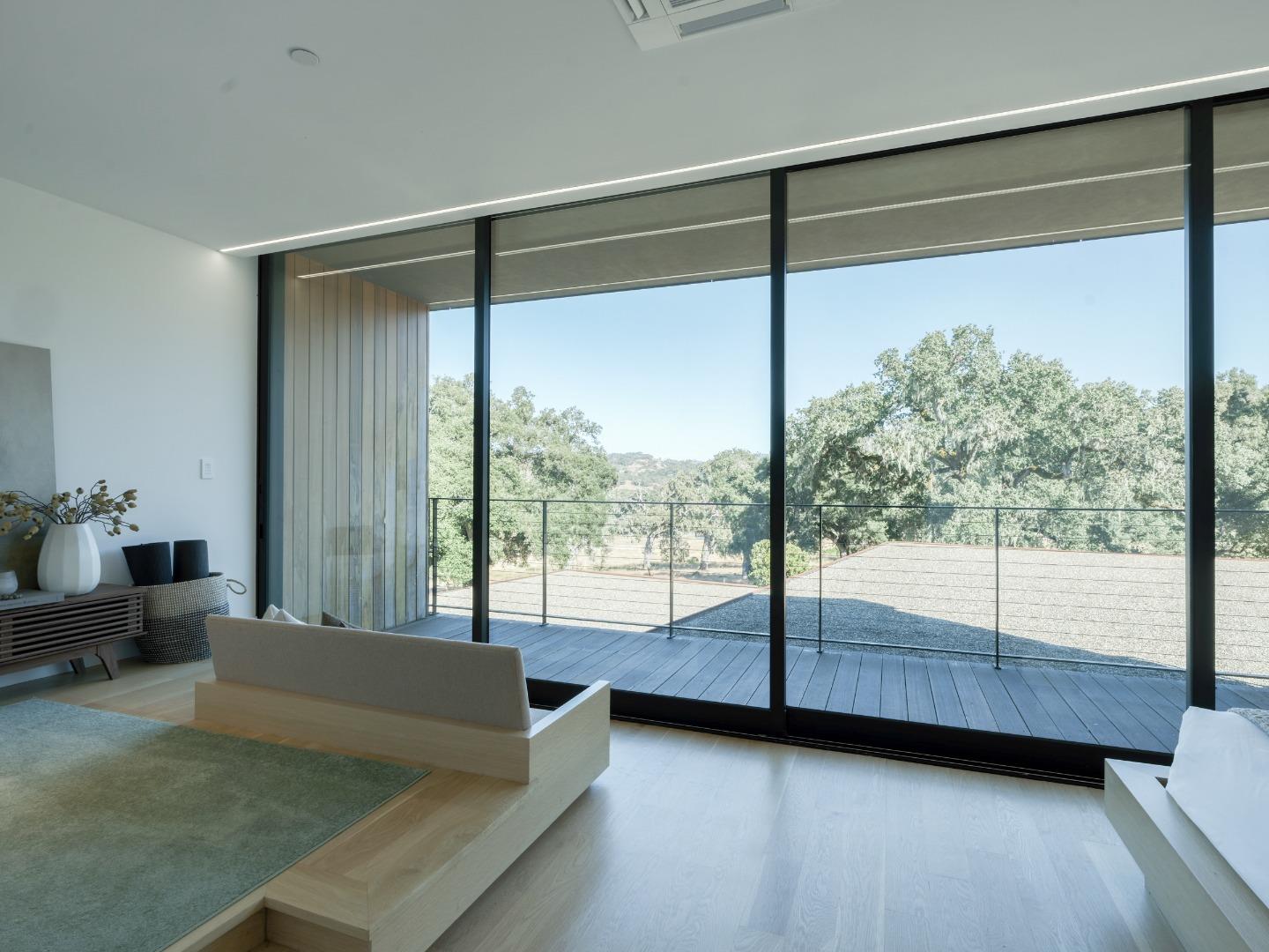Modern living room with expansive glass doors overlooking mature trees and a hillside.
