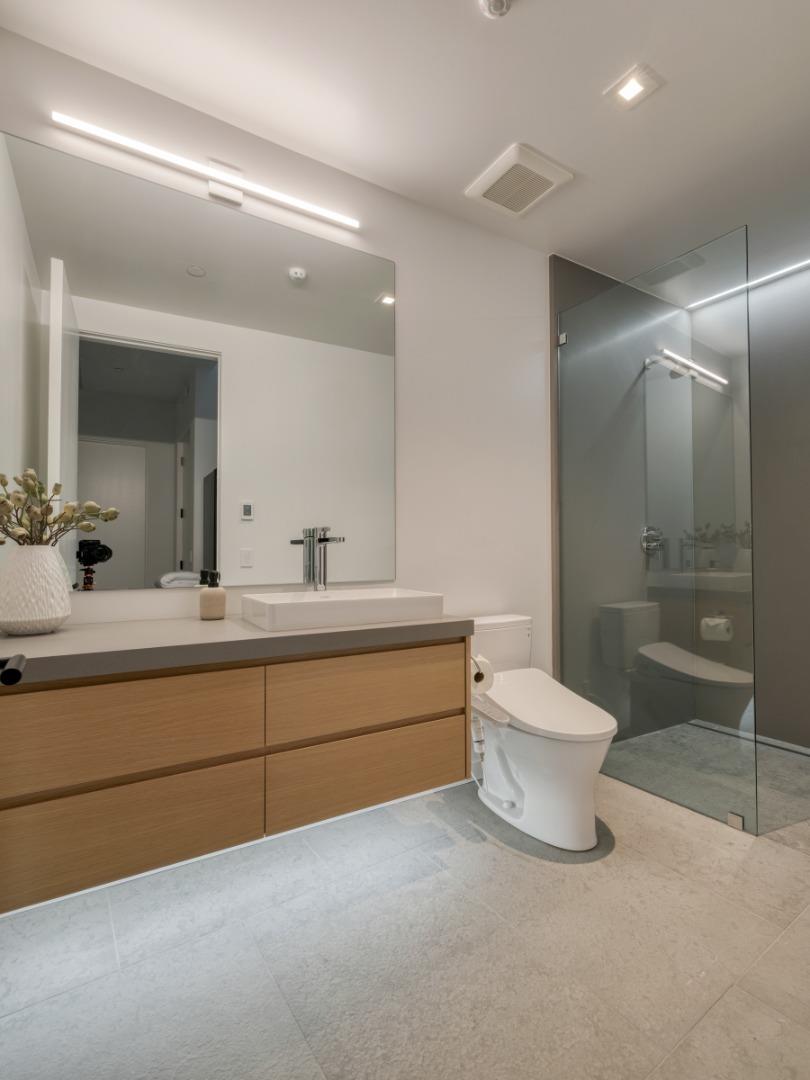 Modern bathroom with a wood-front vanity, wide mirror, and glass-enclosed shower.