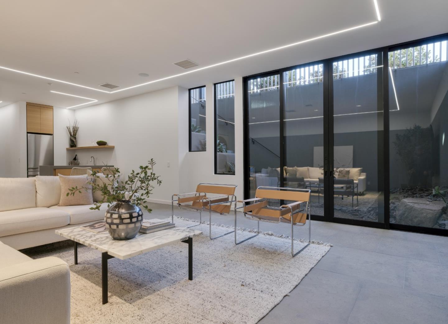 Staged modern living room with cream seating, marble coffee table, and floor-to-ceiling glass doors.