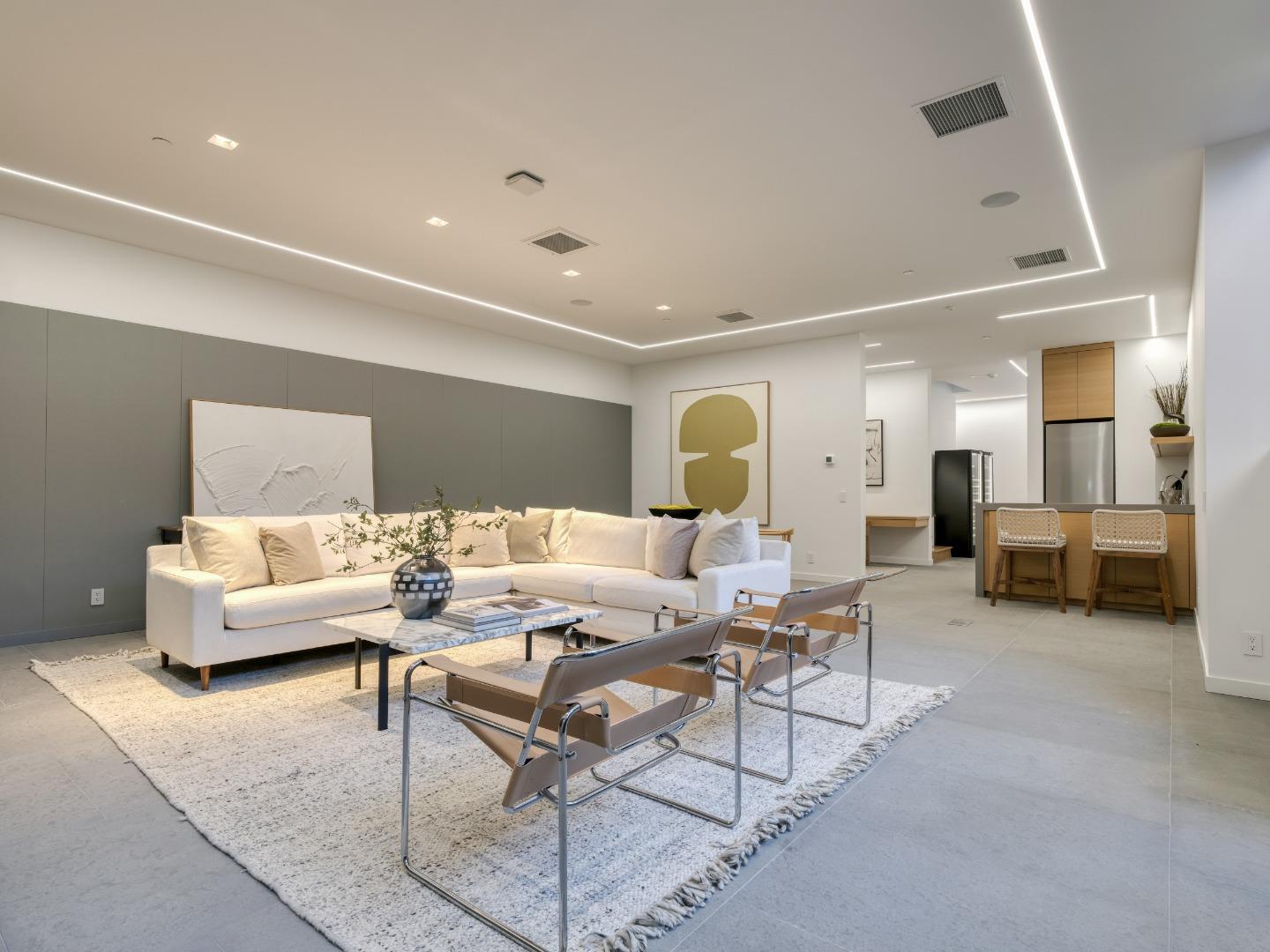 Living room with a white sectional, abstract art, and an adjoining kitchen with woven bar stools.