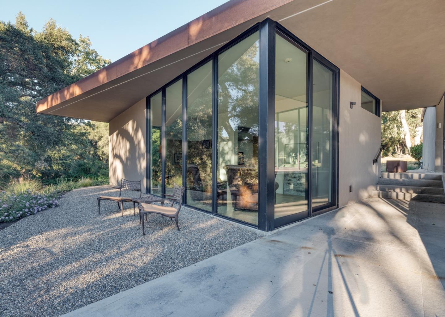 Modern home with floor-to-ceiling corner windows and a gravel patio with lounge chairs.