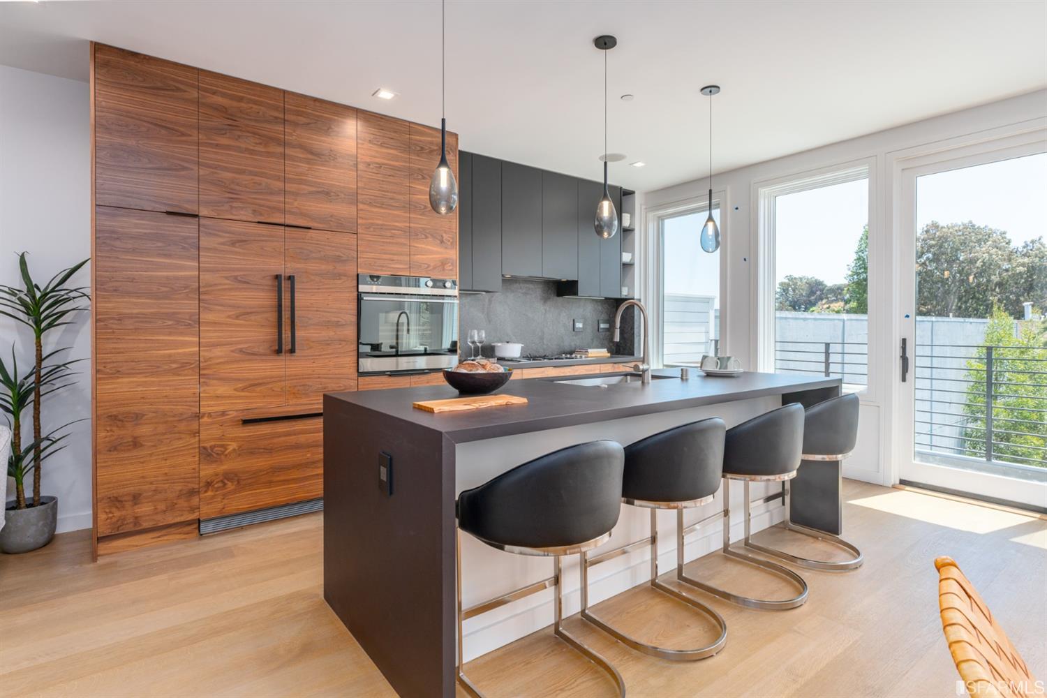 Modern kitchen with walnut cabinetry, a large island, four bar stools, and balcony doors.