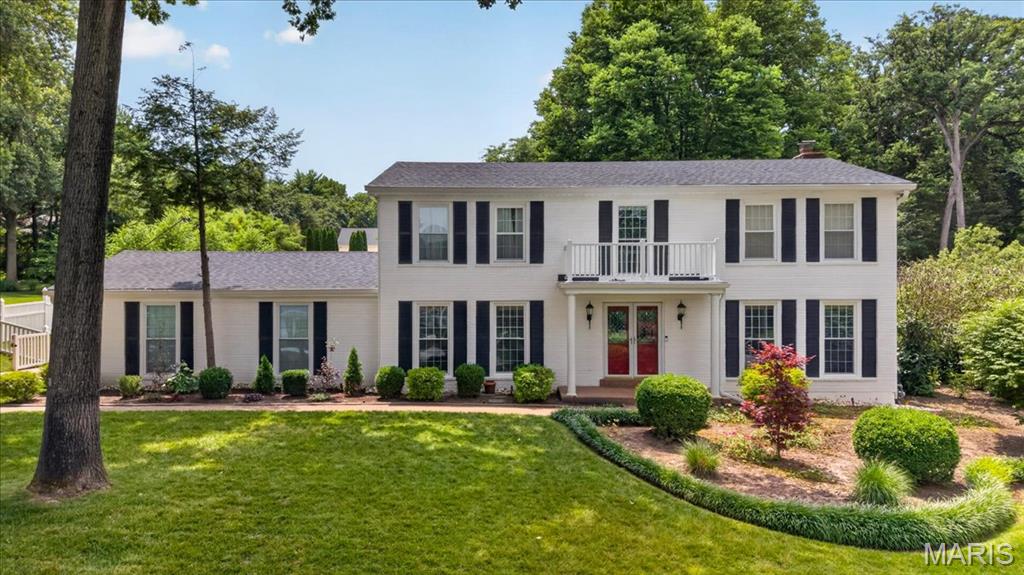 White two-story house with black shutters, a central balcony, and red double doors.