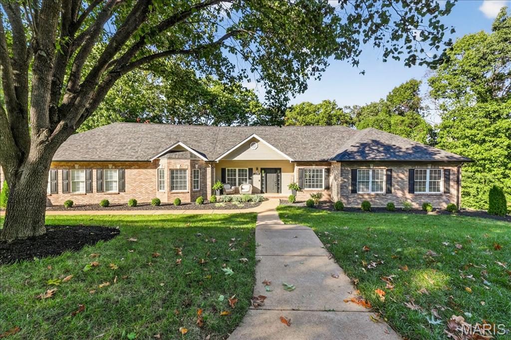 Single-story brick-and-siding home behind a lawn, framed by a large tree and a concrete walkway.