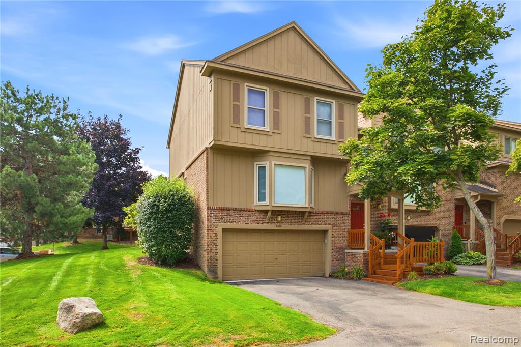 Townhouse with a double garage and wooden porch beside a leafy lawn.