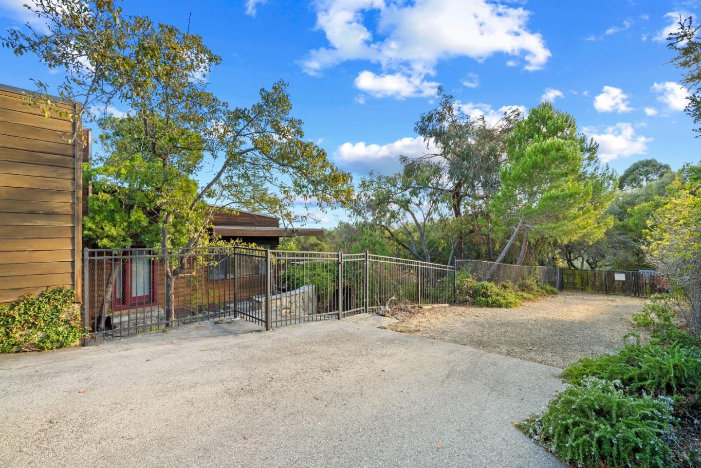 Home exterior and gated driveway bordered by mature trees and shrubs.