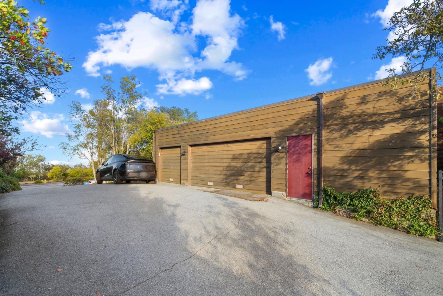 Wood-sided garage with two garage doors, a red side door, and a paved driveway.