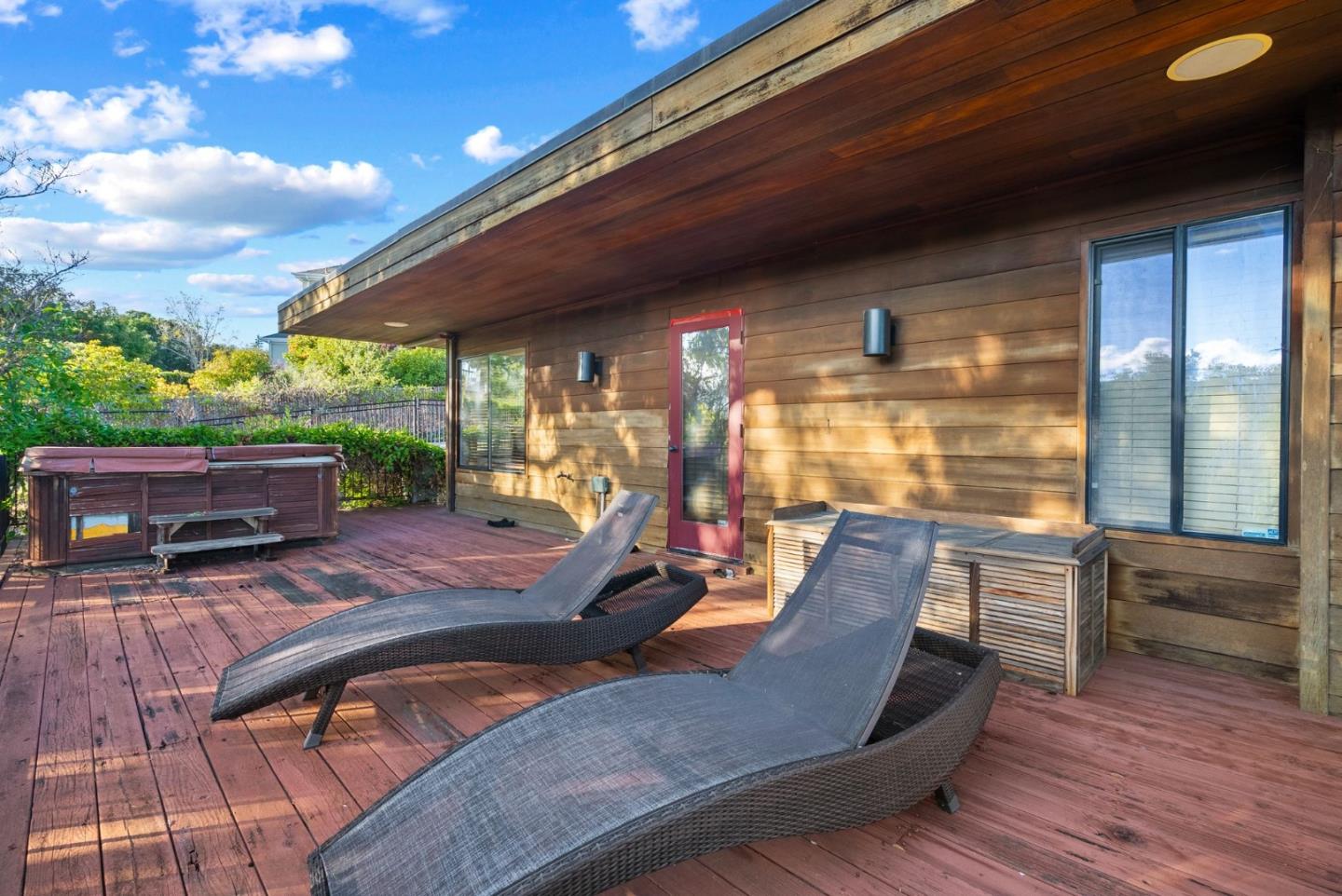 Wood deck with a hot tub and two chaise lounges beside the home.