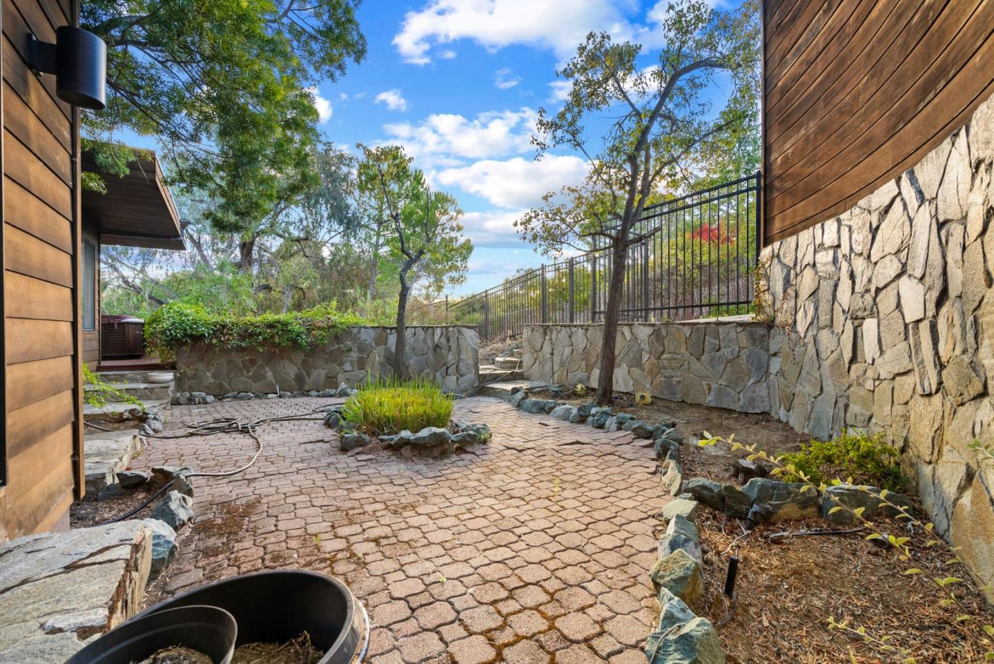 Outdoor patio with brick pavers, stone retaining walls, and a black metal fence.