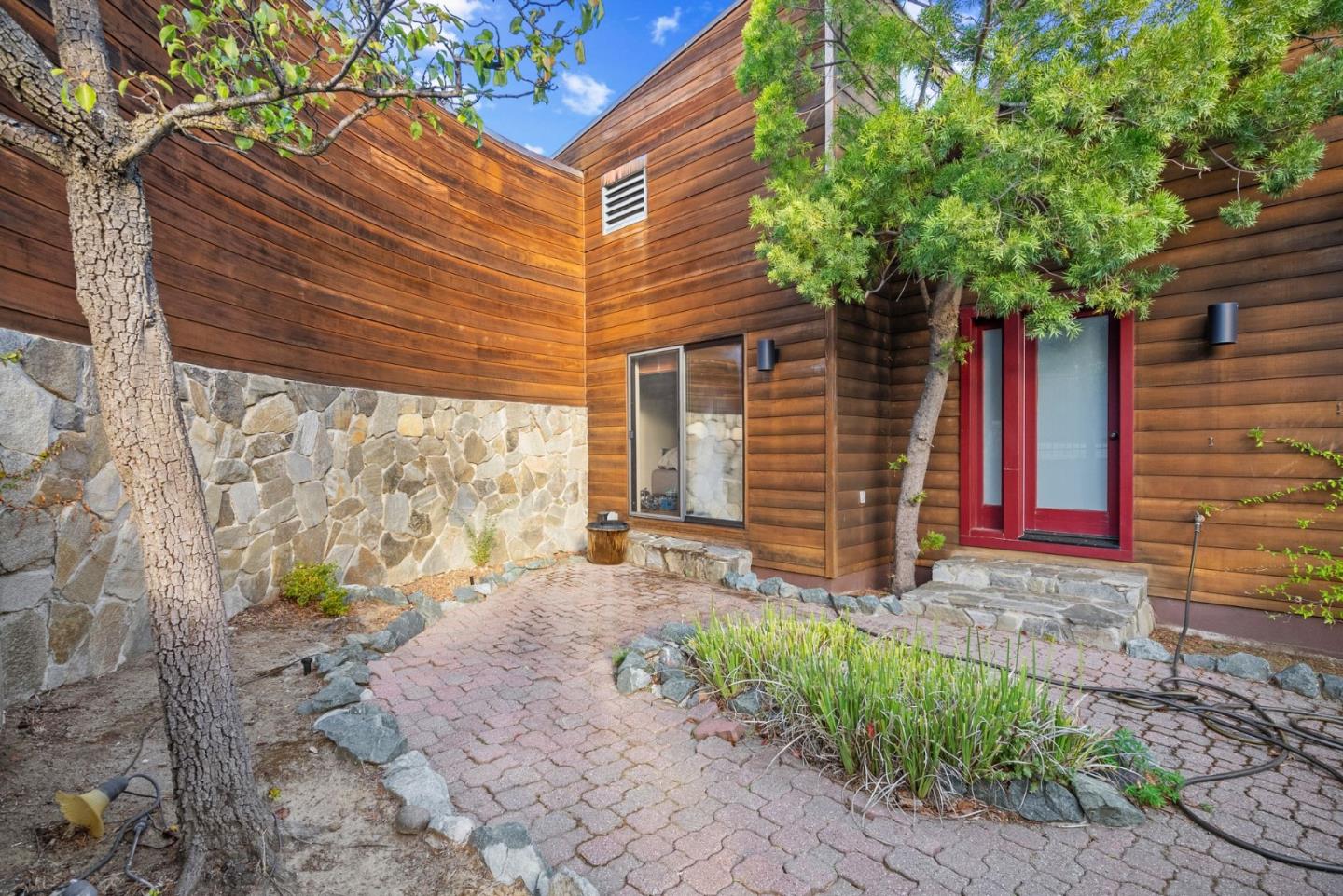 Wood-sided home with a red-framed glass door, stone base, and brick garden path.